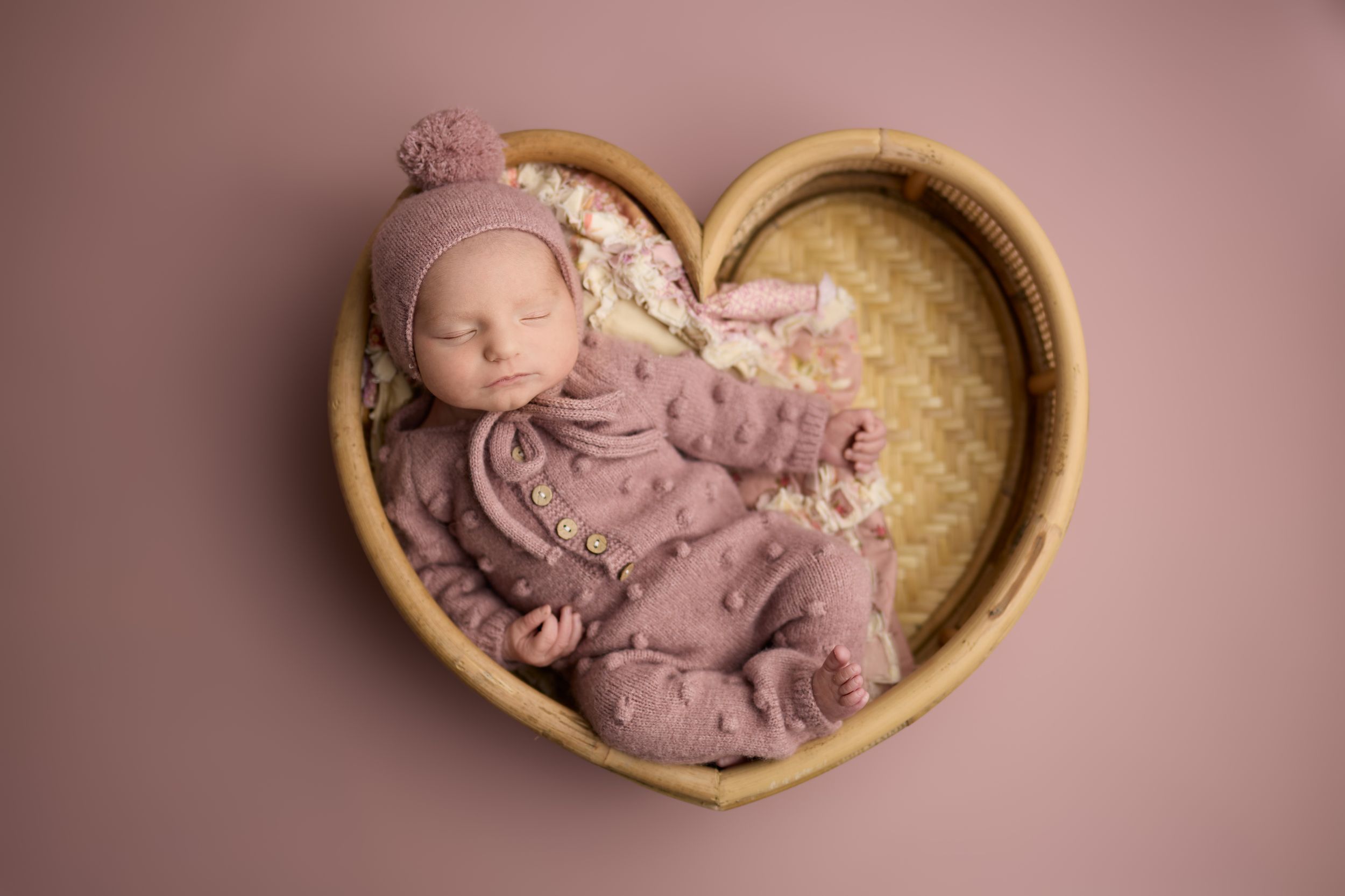 A series of seven wood heart shaped bowls with sleeping newborns are arranged horizontally for a photo portrait session.