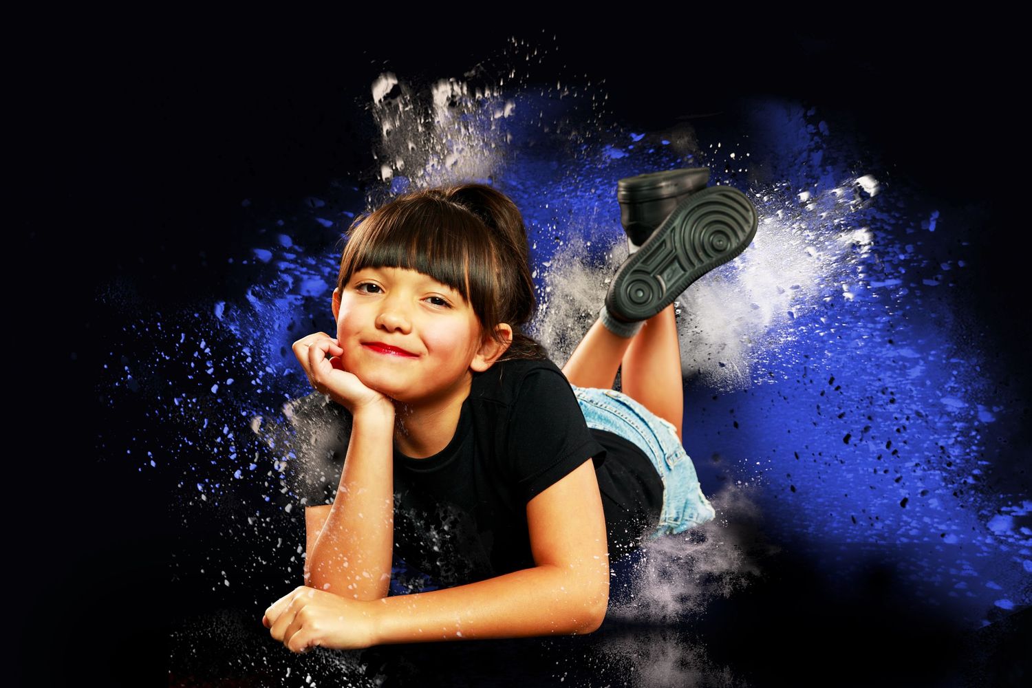 Cheerleader in dark uniform leaps through dramatic gold powder explosion effect against black background.