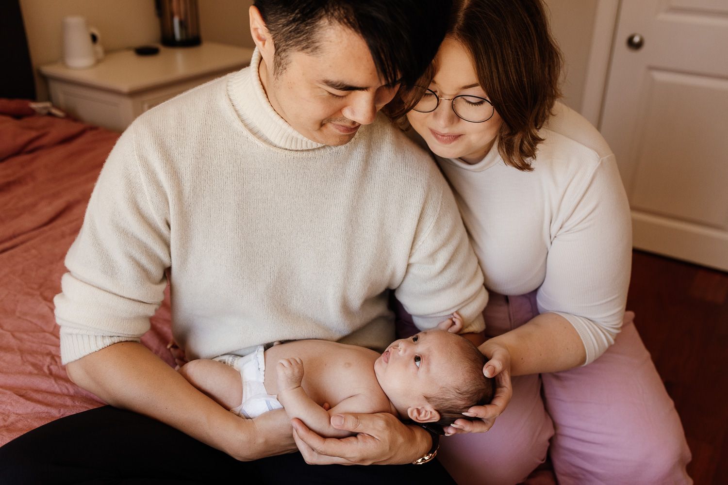 A tender family moment captured in warm tones as parents feed and bond with their baby at home.