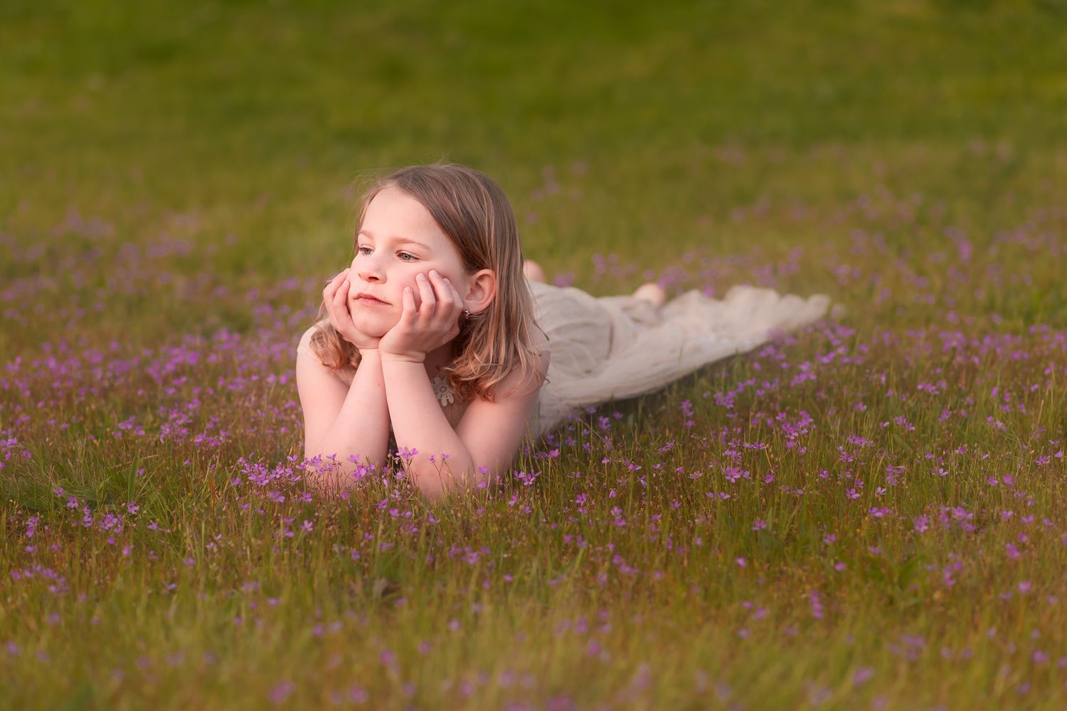 A woman lying on grass gazes wistfully among spring wildflowers in a dreamy outdoor scene.