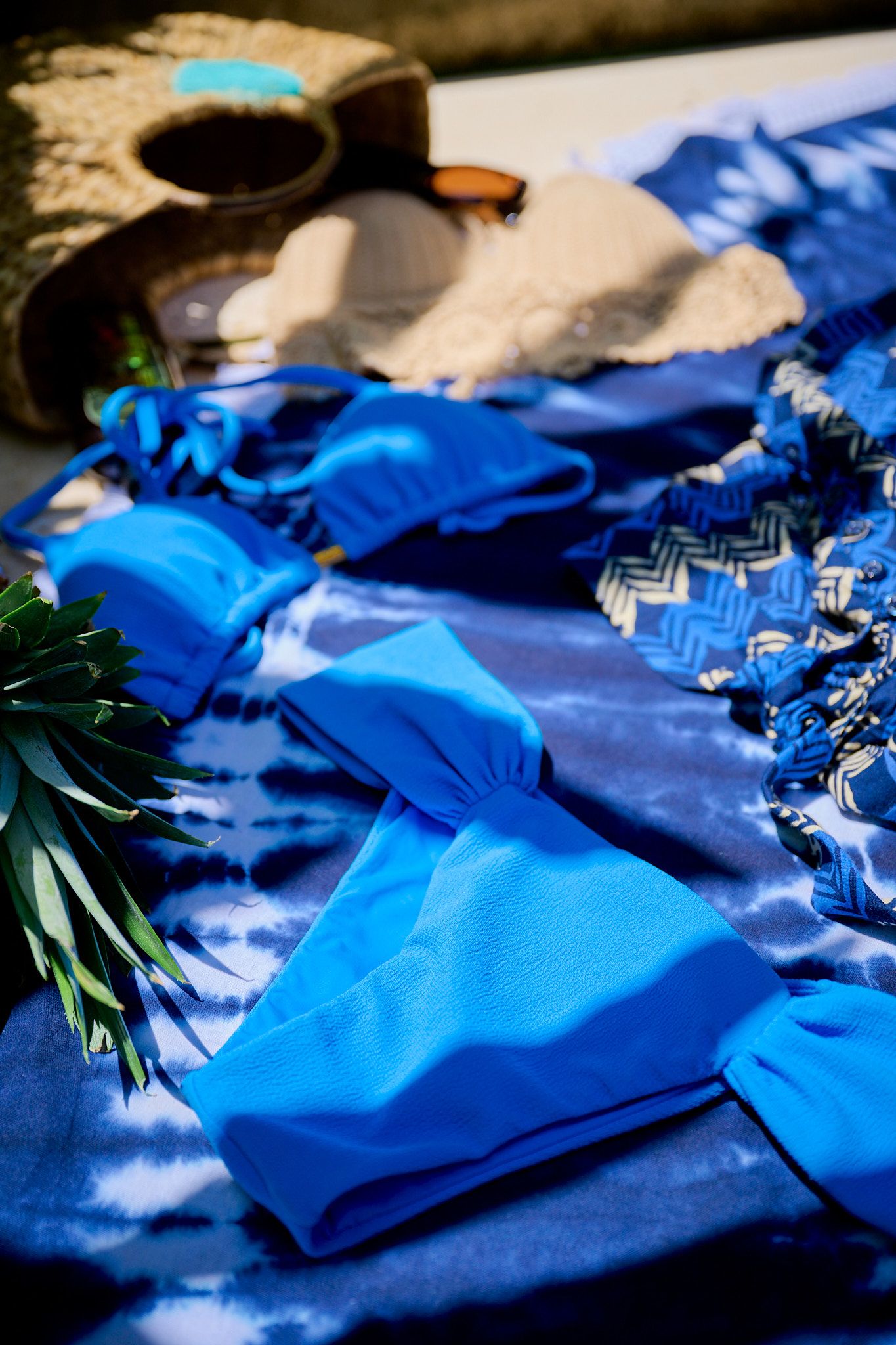 Vibrant blue tie-dye fabric laid out with various clothing items and a plant in natural sunlight.