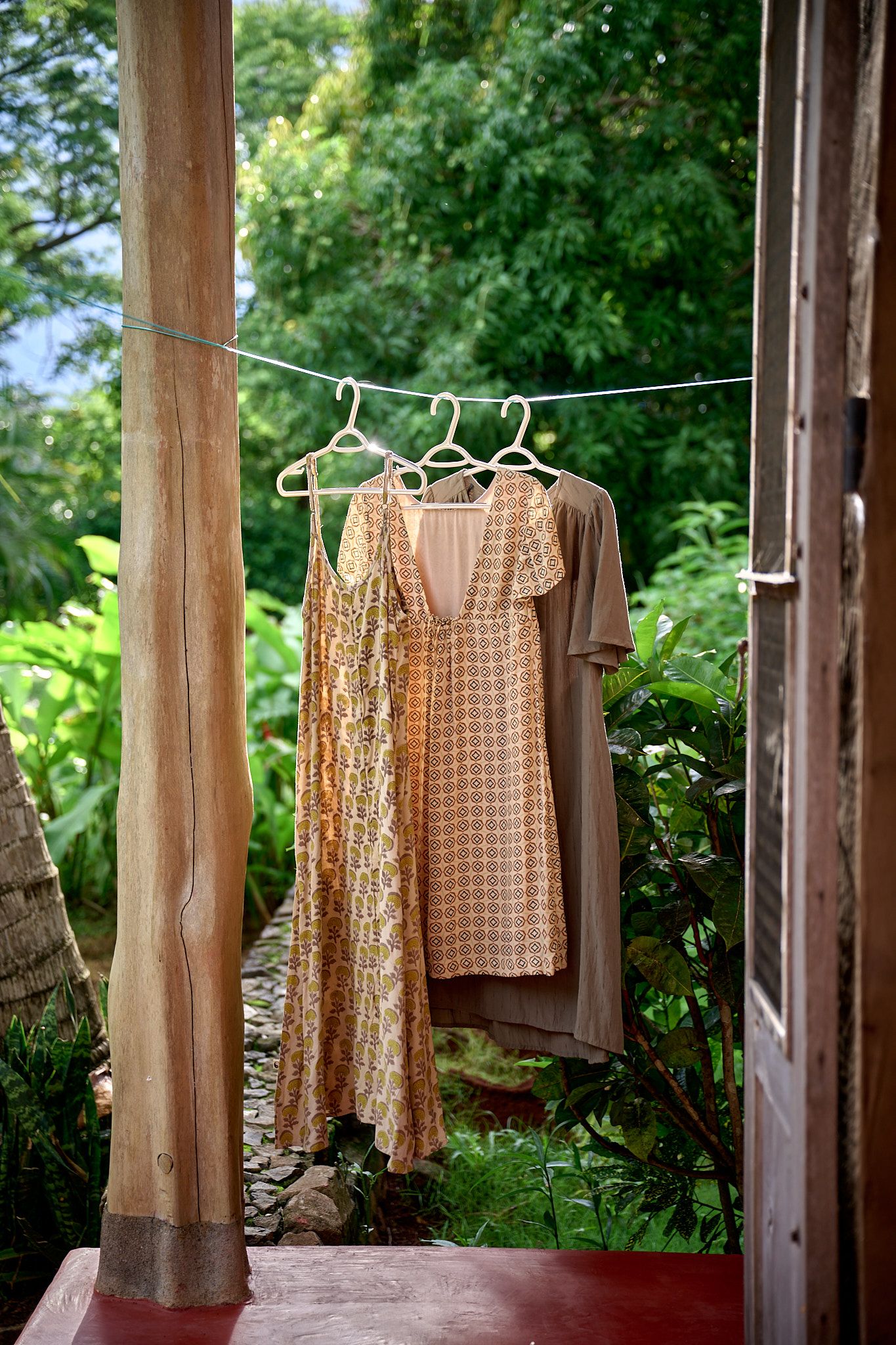 A series of vintage blush and neutral colored dresses hanging on wooden hangers in a rustic outdoor setting.