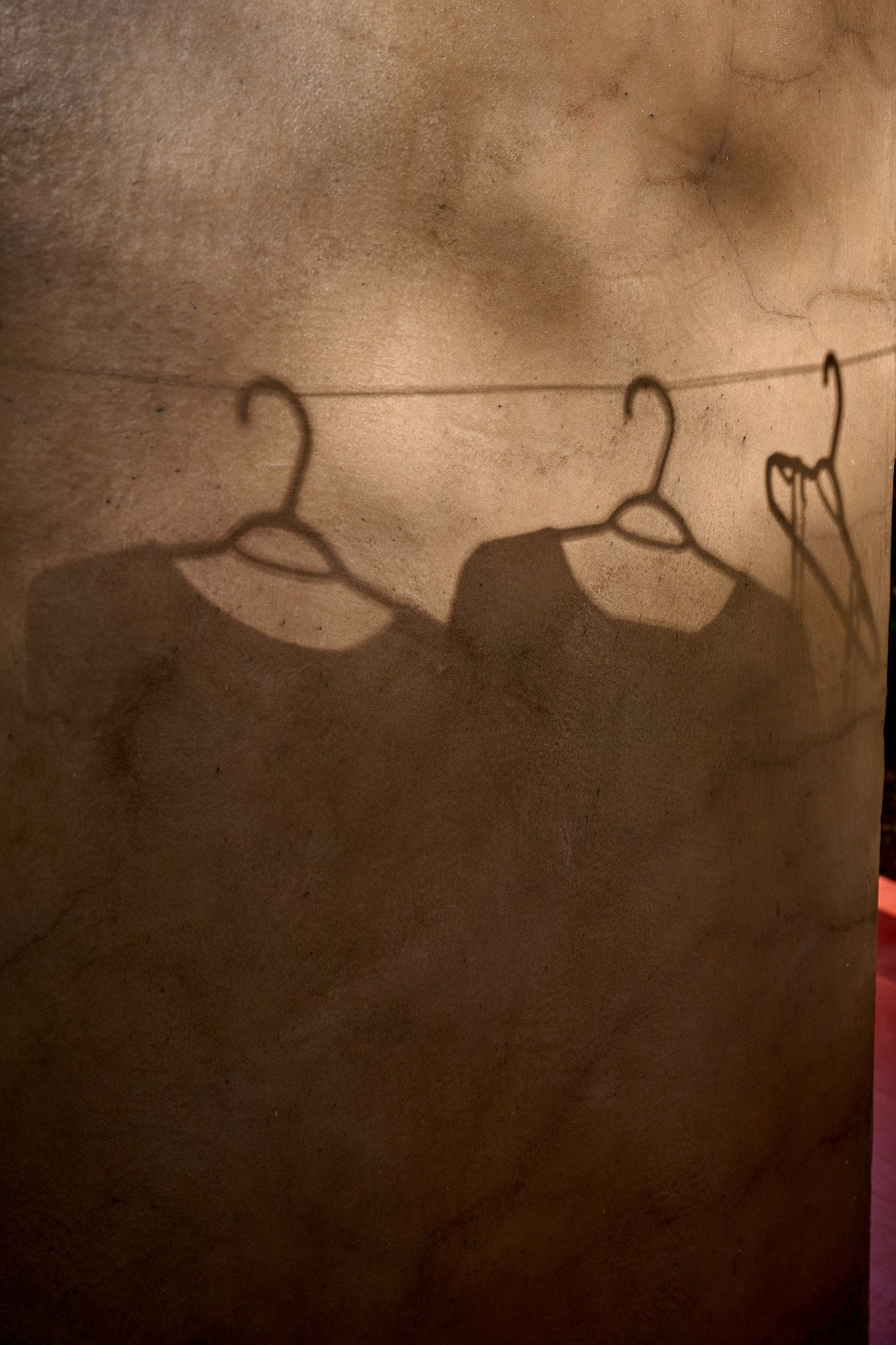 Shadows of empty coat hangers cast dramatic silhouettes against a textured brown wall.