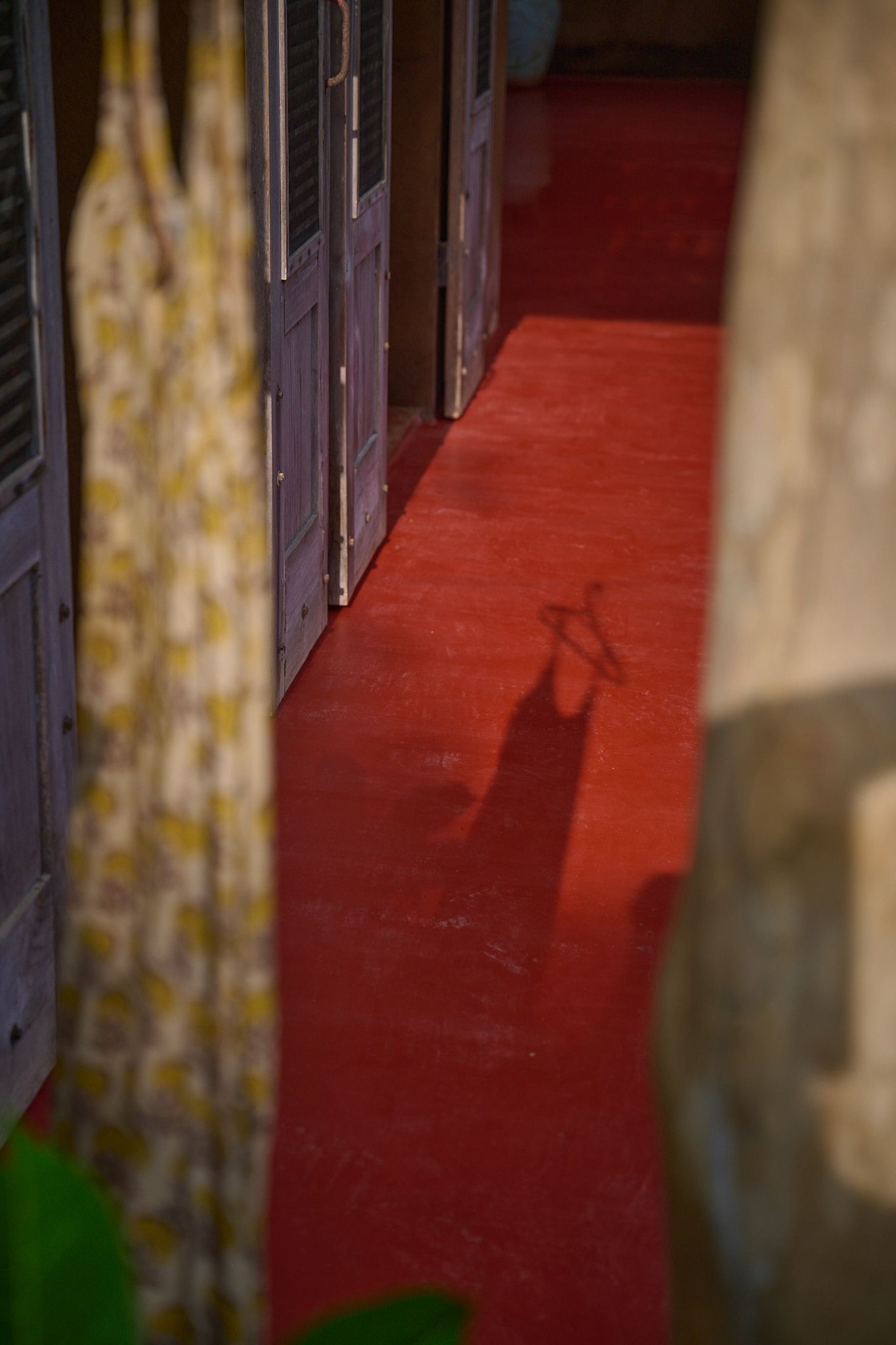 A shadow of a person cast on a red floor beside curtains and window frames.