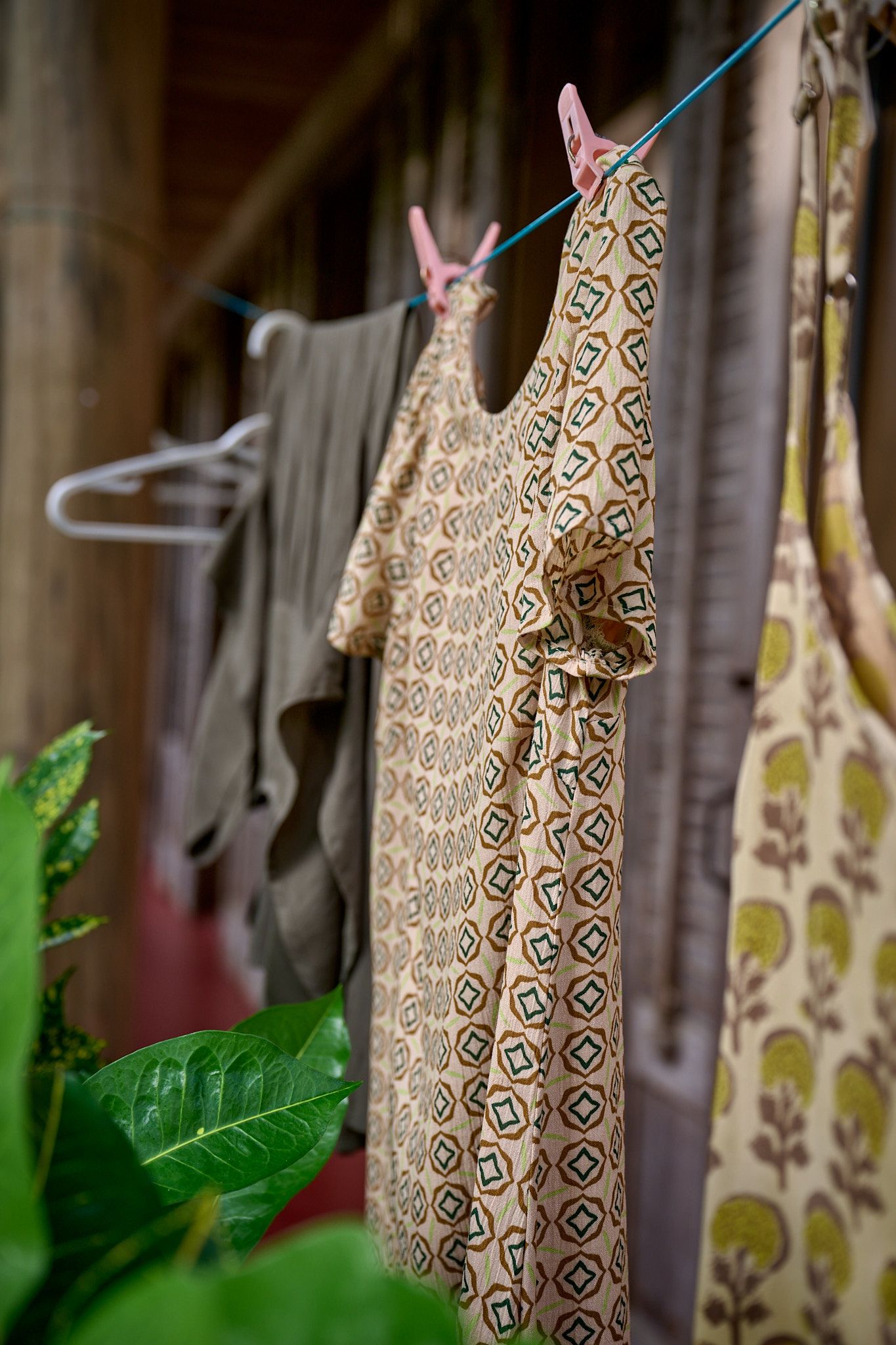 Clothes hanging on a laundry line with patterned dresses and garments visible among green leaves.