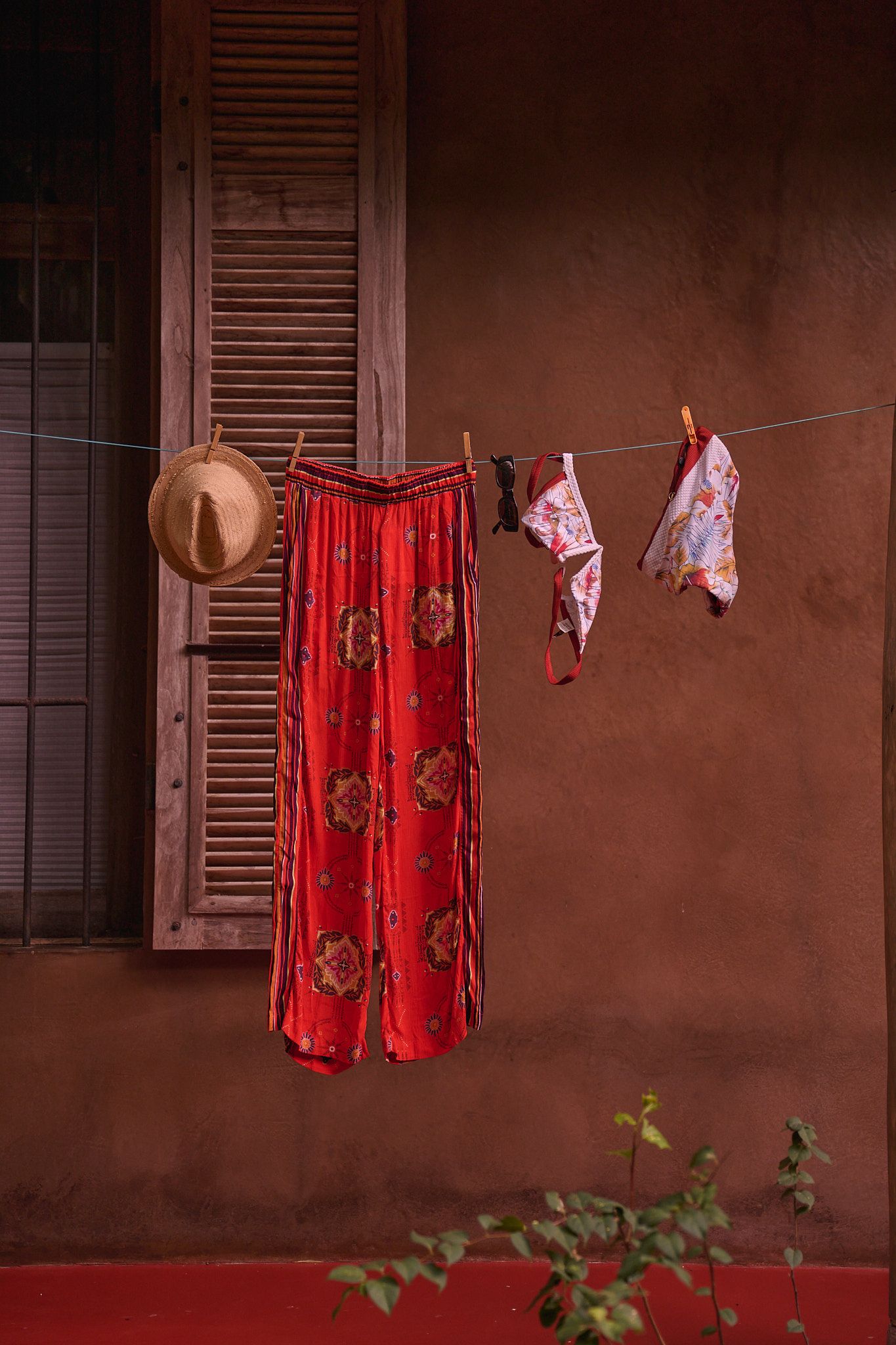 Red clothing hangs on a clothesline against a rustic brown wall with shuttered windows creating a dramatic scene.