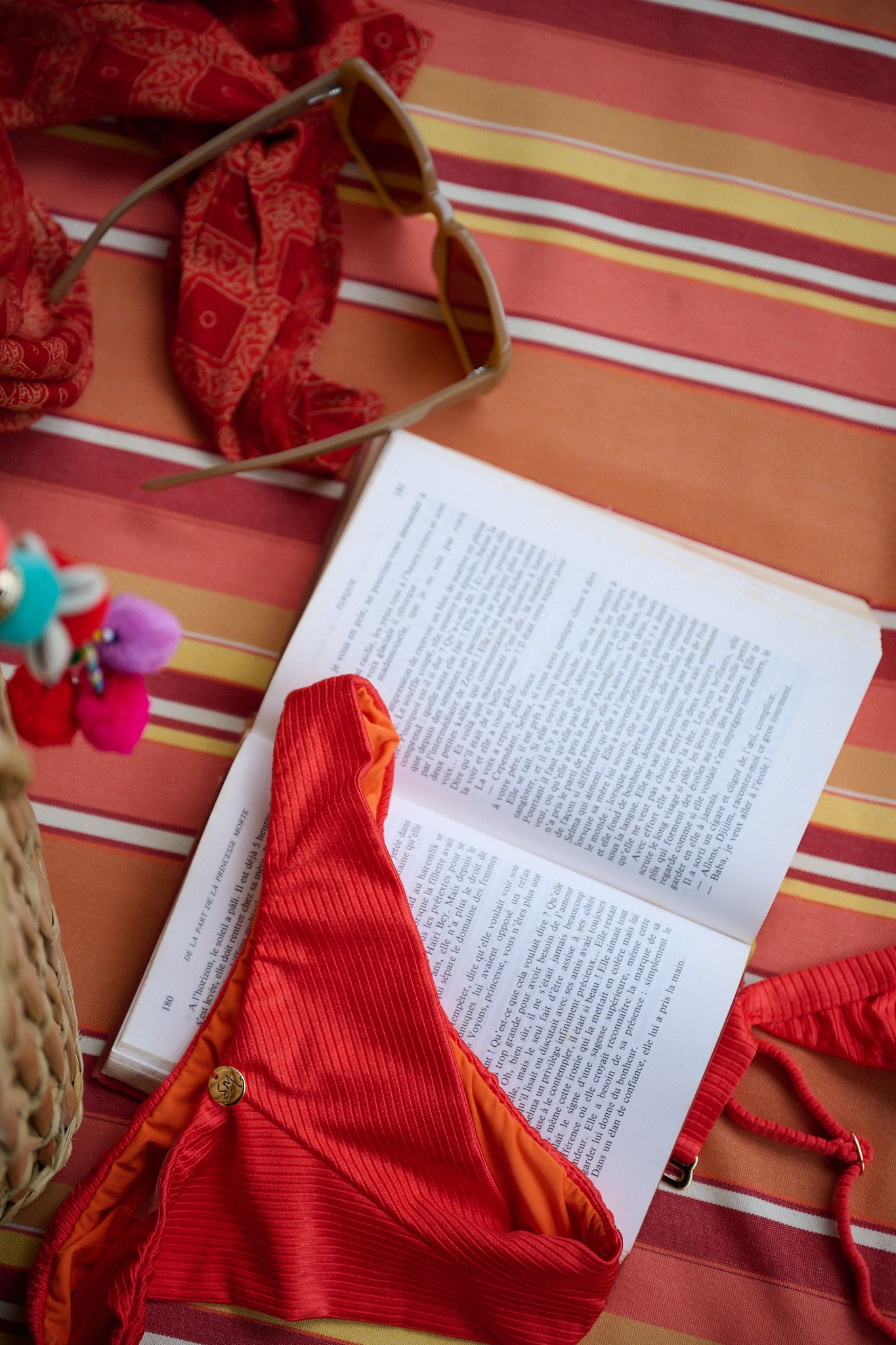 An open book resting on a striped surface with a red article of clothing and floral decorations nearby.
