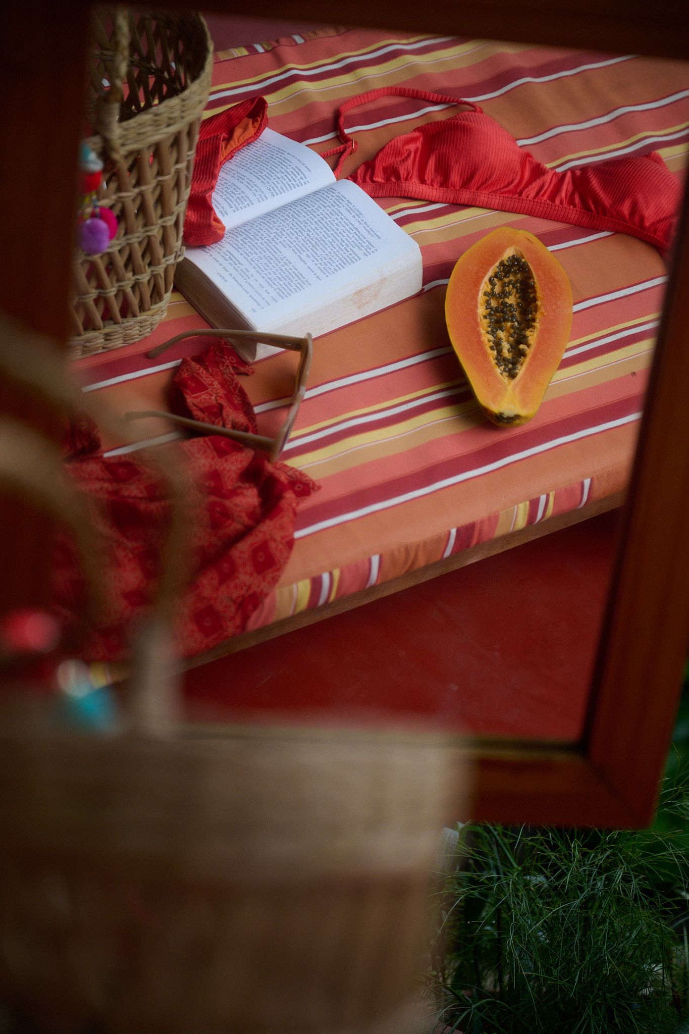 Half-cut papaya and open book rest on striped orange fabric with rustic woven decor in foreground.