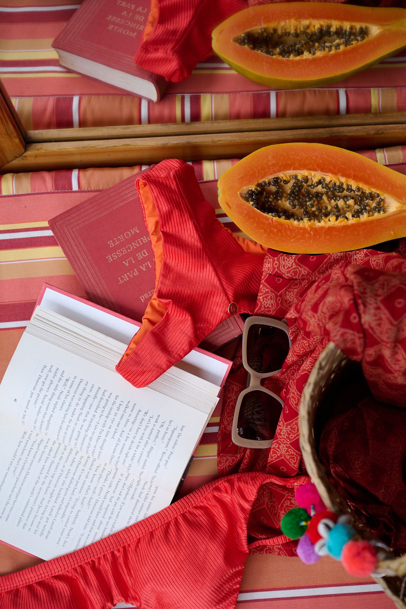 Book pages and text beside a sliced papaya fruit with dark seeds on a red cloth background.