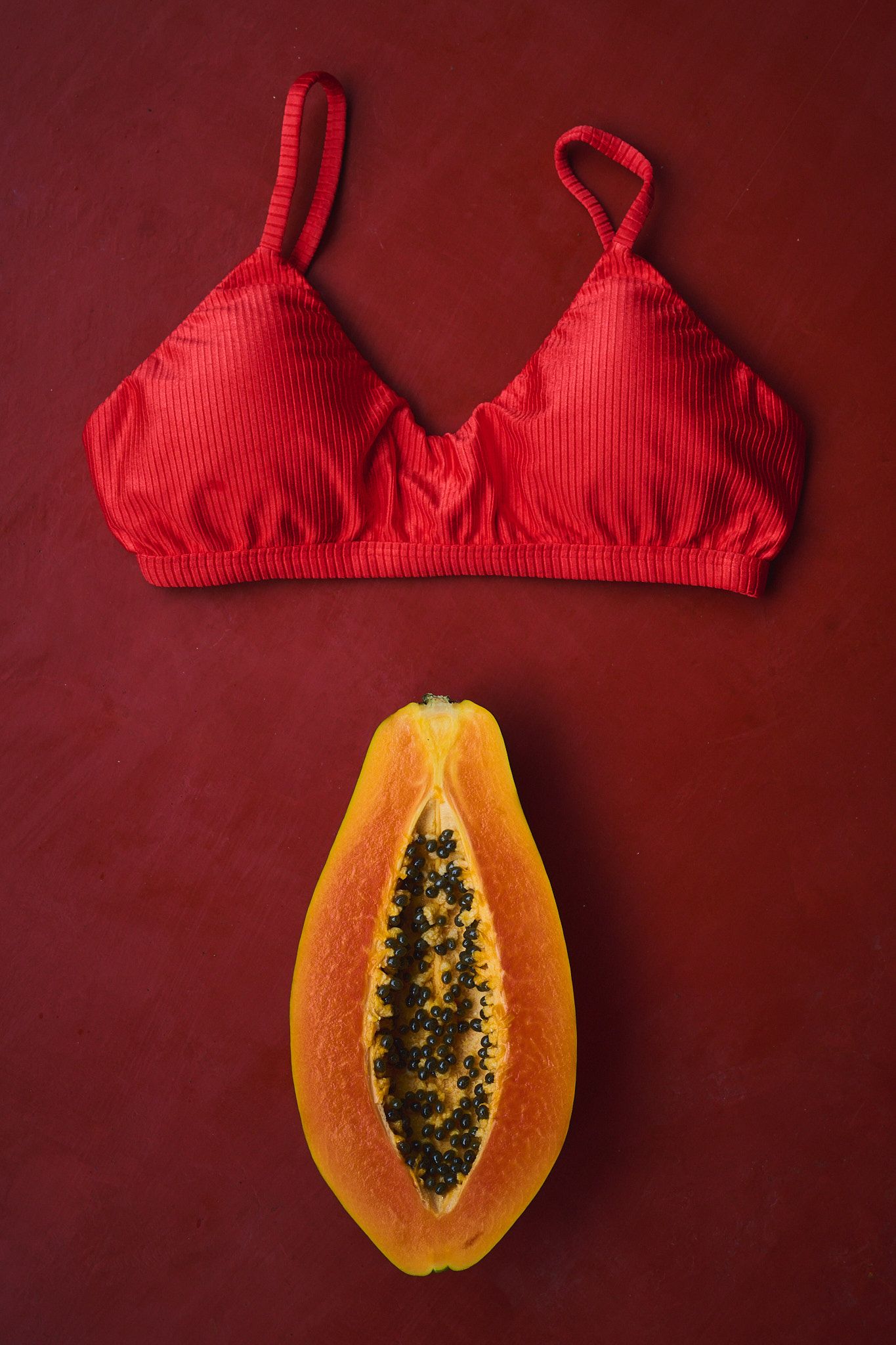 A sequence of images showing the visual comparison between red bikini tops and papaya fruit halves lined up on a dark red background.