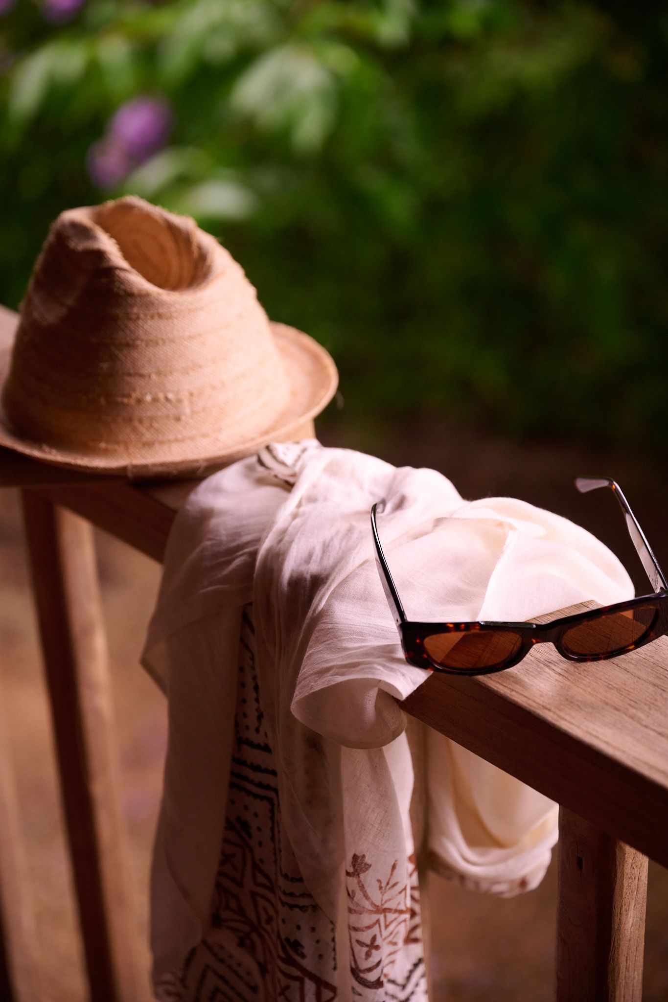 A white sunhat with gauzy fabric trim and sunglasses rests elegantly on a wooden surface in soft lighting.