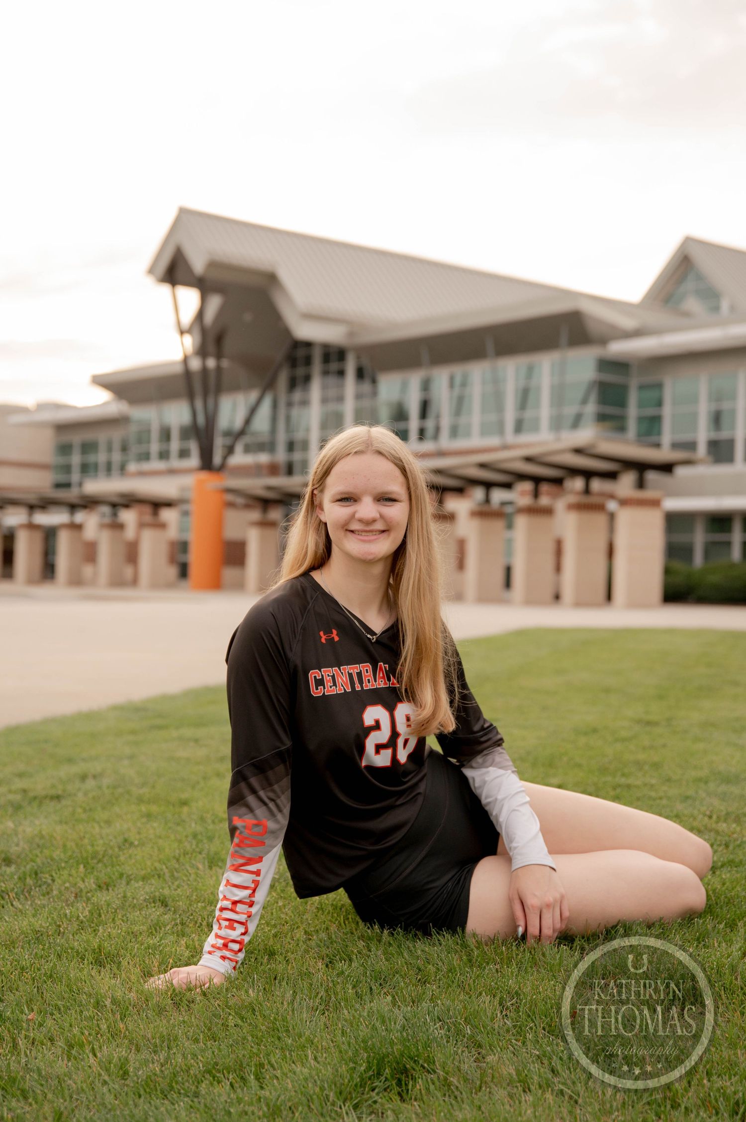 Student athlete in black jersey reclining on grass field at modern school campus.