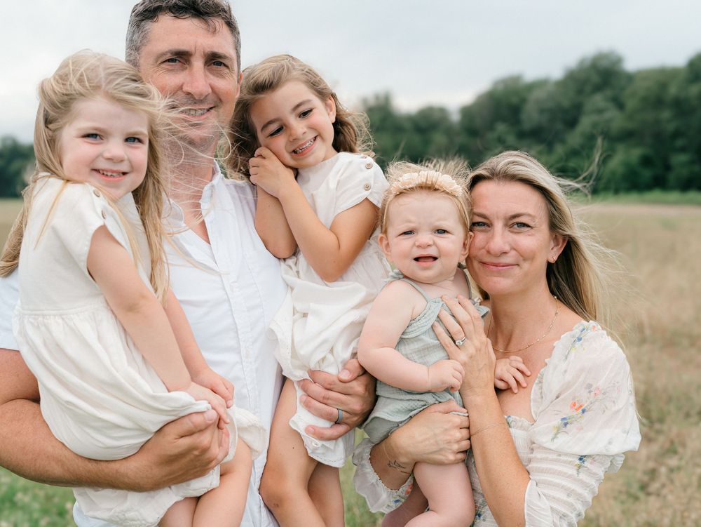 Mom and dad laughing with their three daughters during playful family photo session — natural lifestyle photography in Monmouth County.