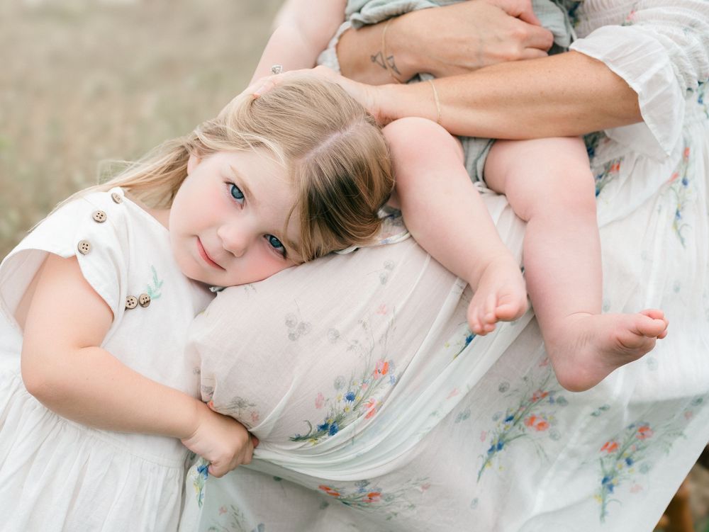 A young girl rests her head on her mother's thighs while smiling.