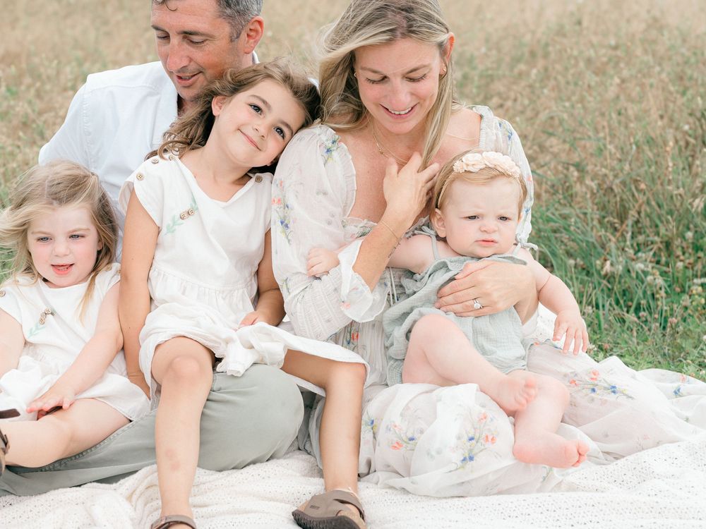 Mom and dad laughing with their children while sitting on a blanket in Monmouth County.