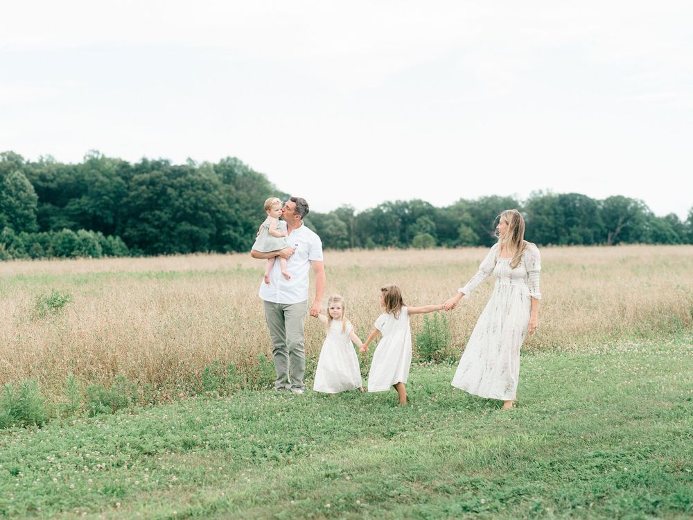 Family of five walking hand-in-hand through a sunlit field in Monmouth County, NJ — candid moment during family photography session.