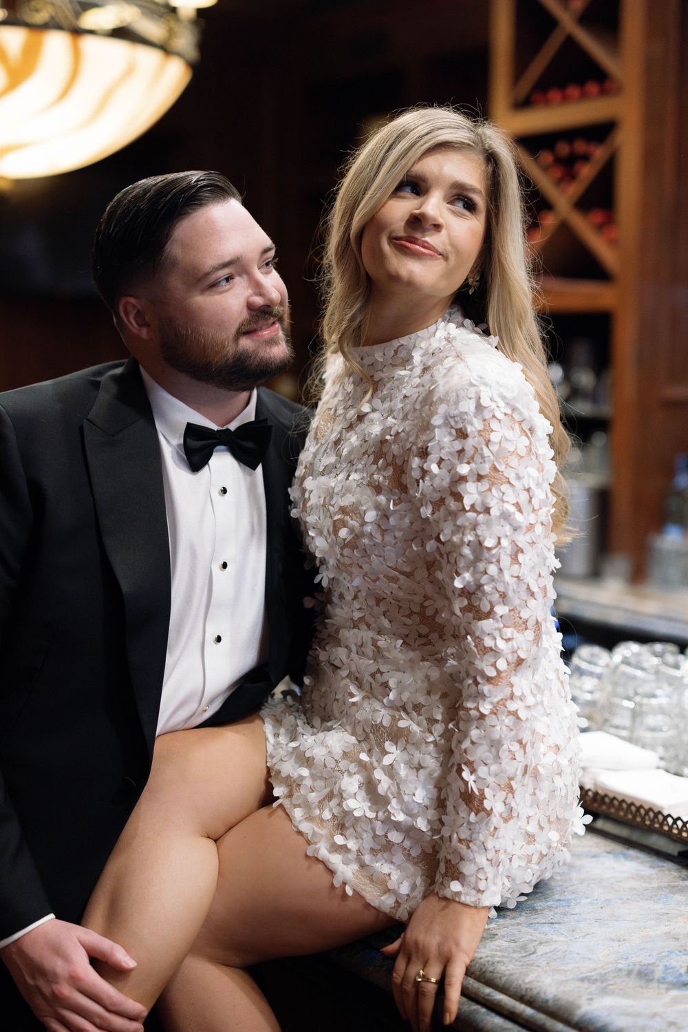 Couple in formal attire poses for romantic wedding photos in a rustic wine cellar setting.