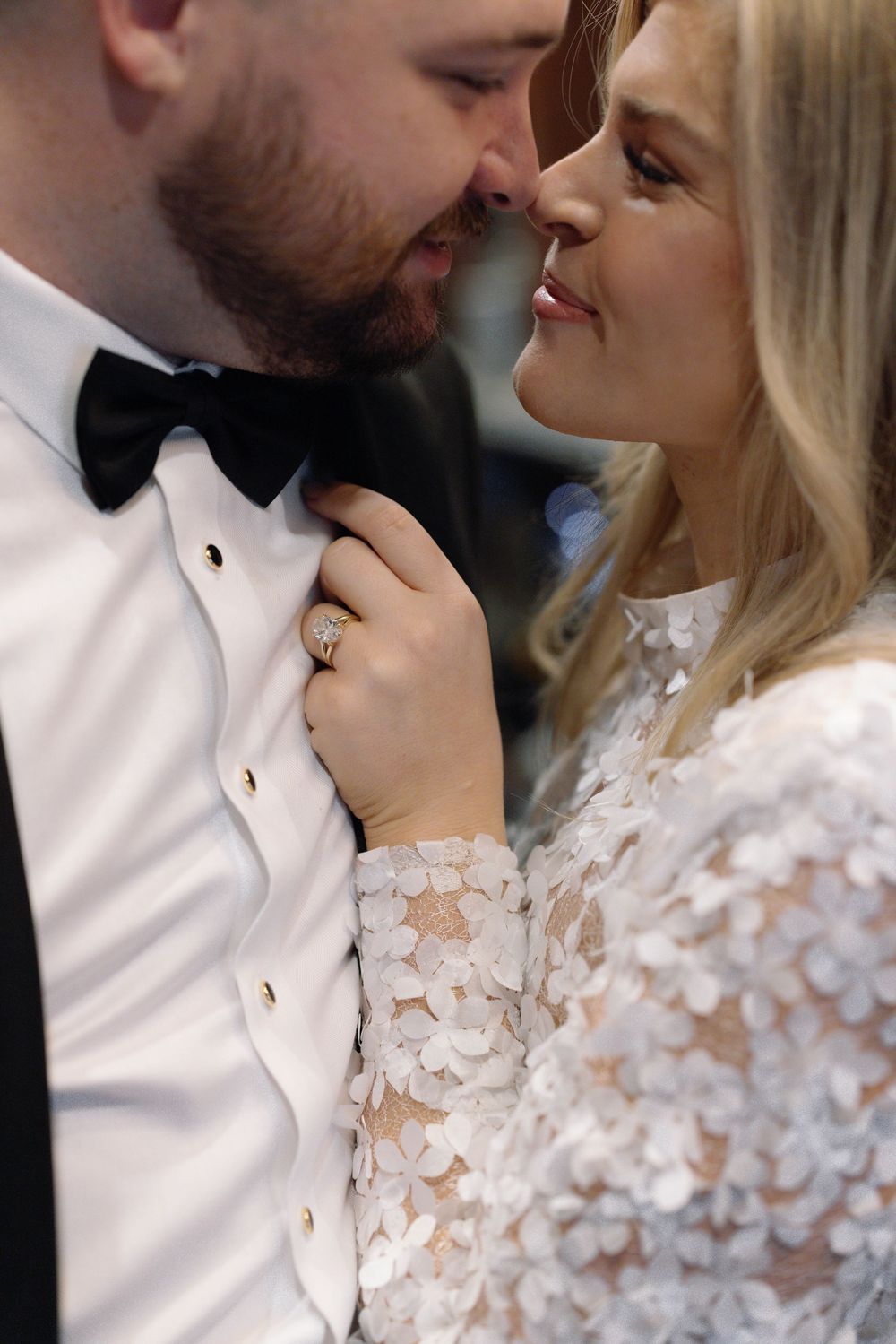 Close up romantic wedding photo showing couple in formal attire with white lace dress and black bow tie.