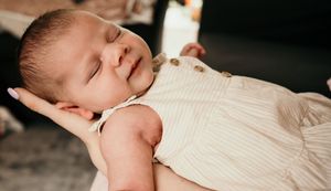 Peaceful sleeping newborn in white dress captured in natural light.