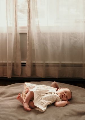 Sleeping infant lying peacefully against soft white curtains in natural light.