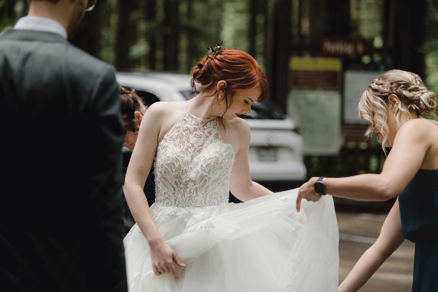 Close-up shot of a bride's flowing white wedding gown being adjusted in a forest setting.