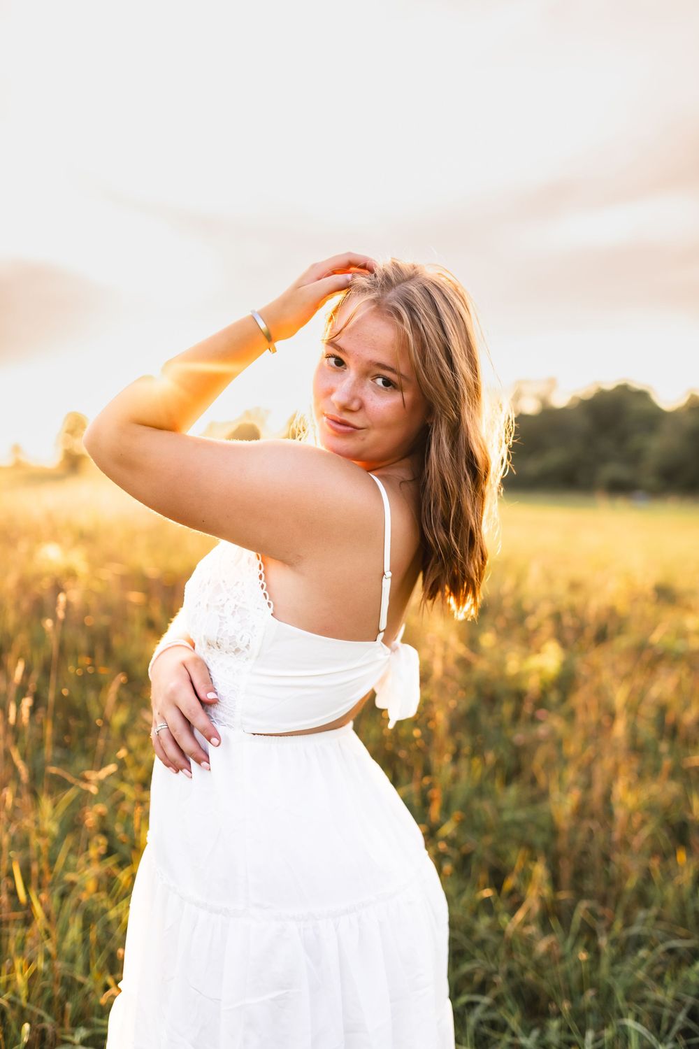A golden hour photo of the sun shining on a senior girl in an open field.