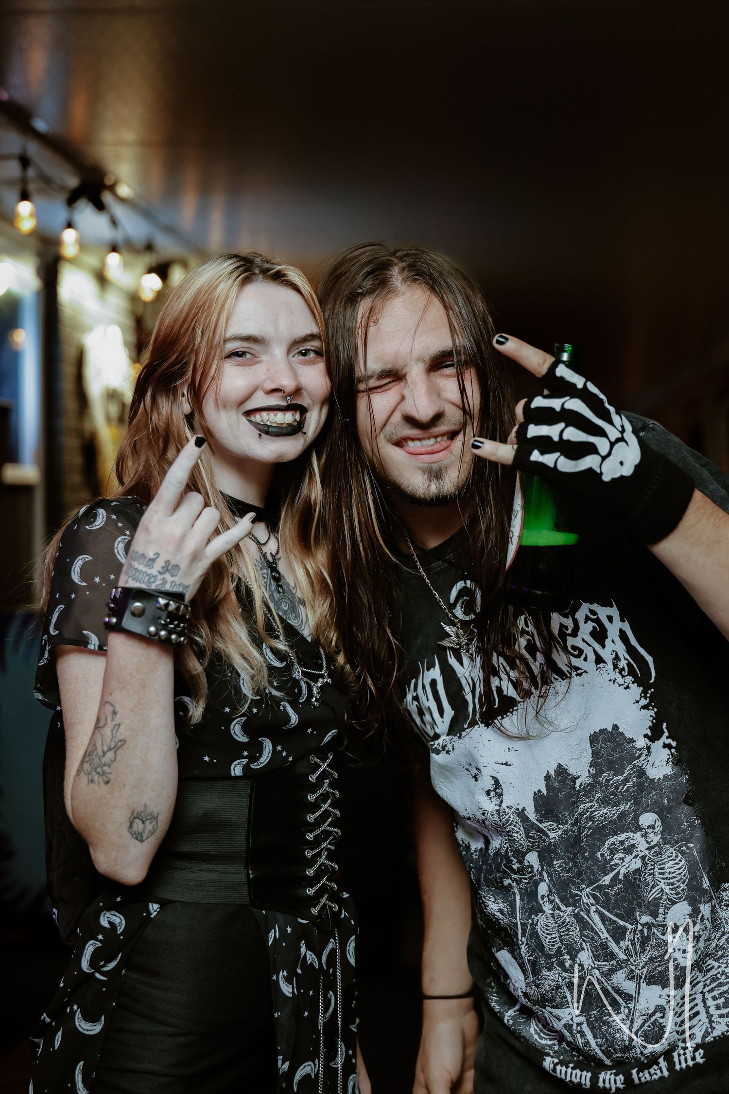 Two metalheads in dark clothing pose together at a rock show.