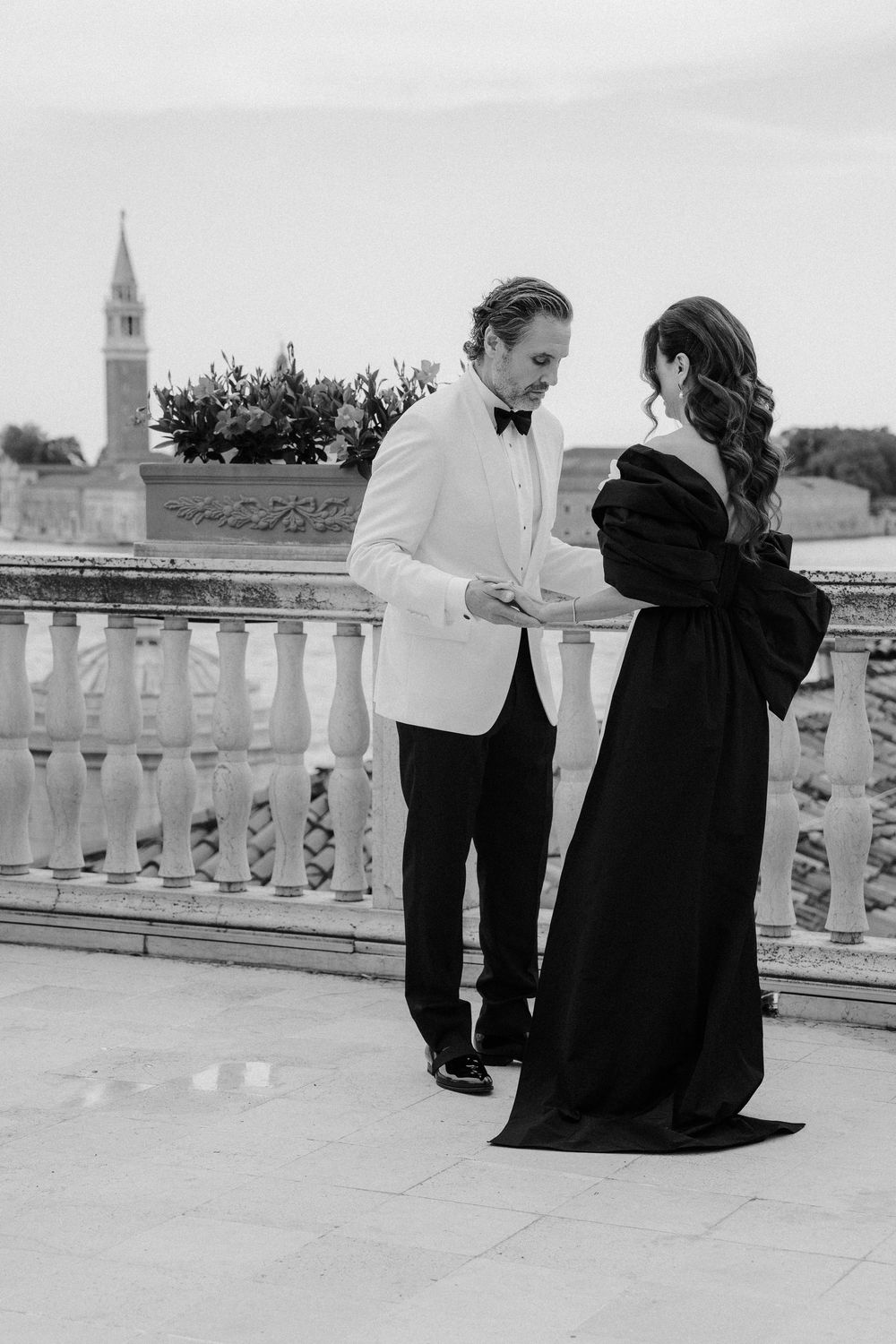 Couple in formal attire sharing intimate moments on a balcony with city views. Photoshoot by Venice Photographer Alina Indi