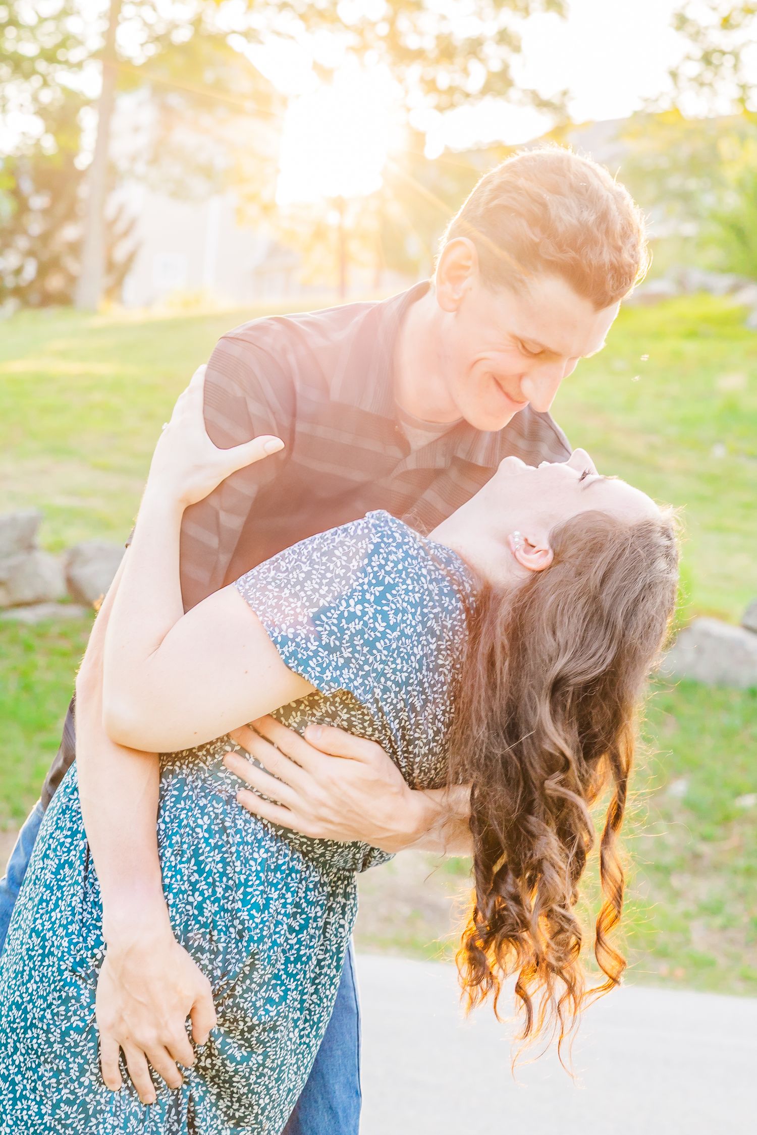 Romantic couple dancing in warm sunset light with woman in floral dress being dipped in graceful pose outdoors.