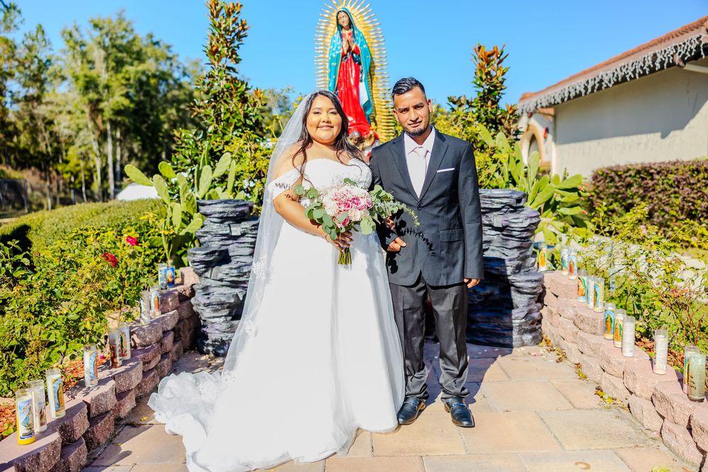 Wedding couple poses for photos in garden path with religious statue in background.