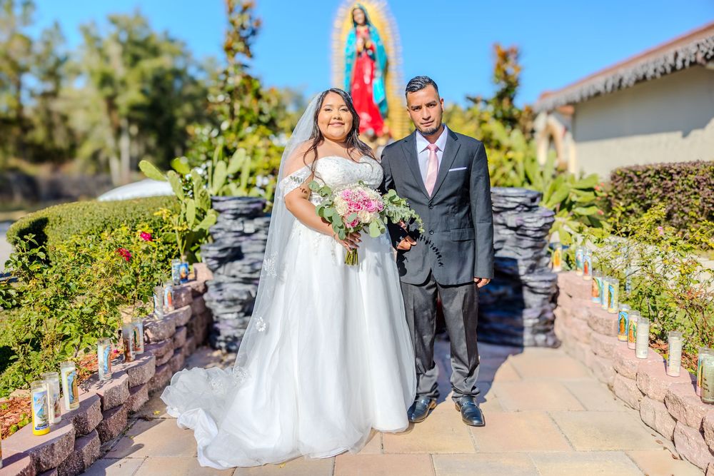 Wedding couple taking portraits on stone pathway with religious artwork and greenery.