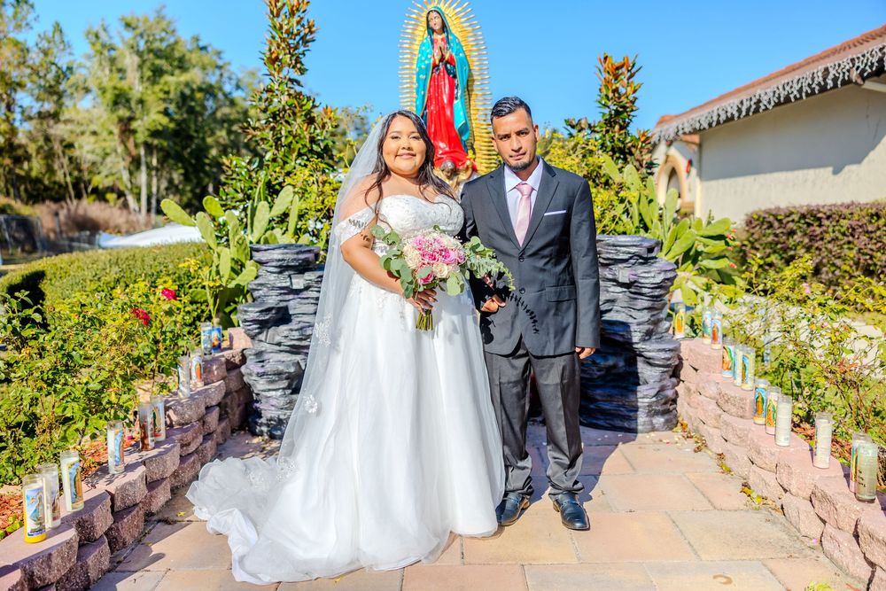 Wedding photo session on garden path with religious statue and landscaping.