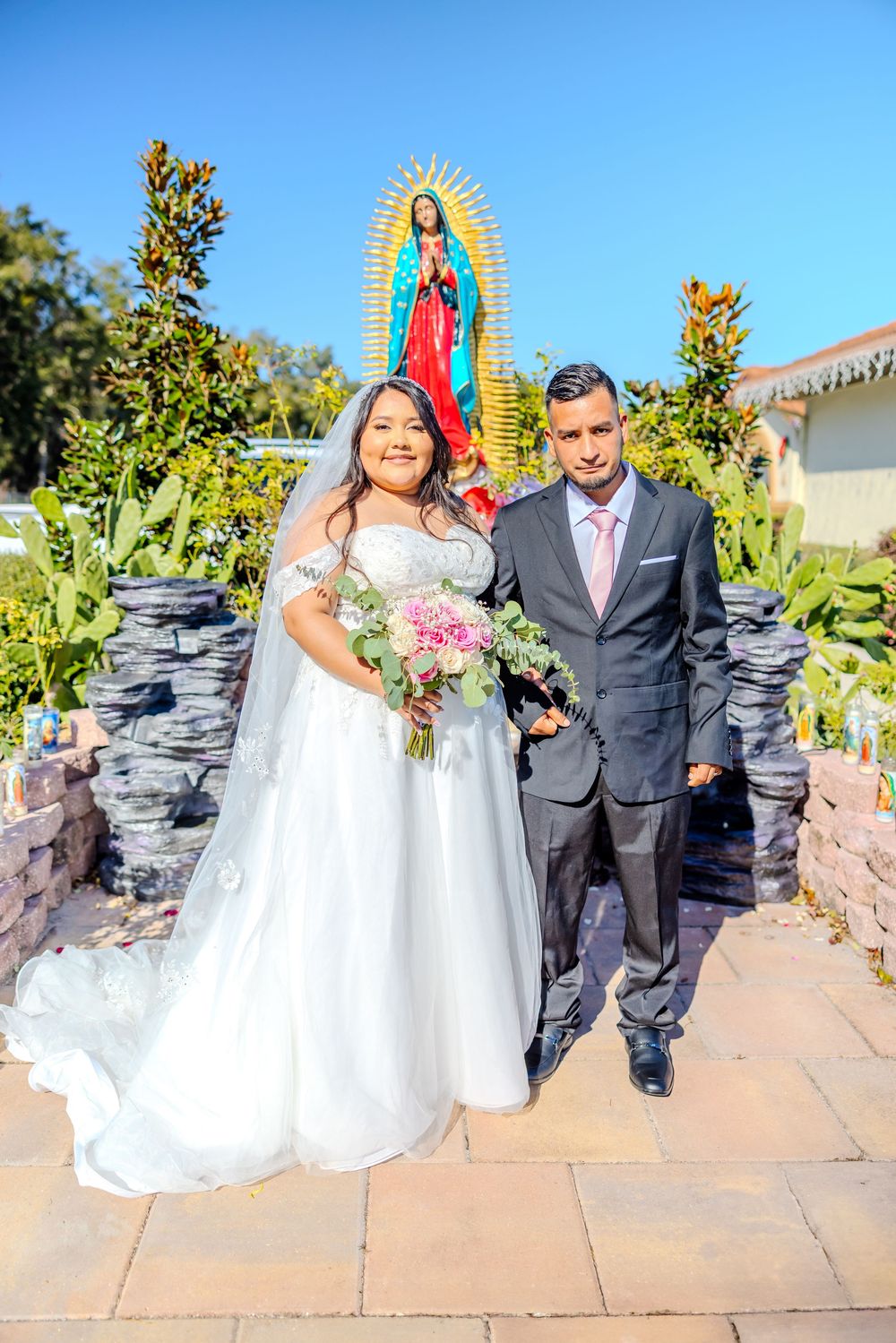 Wedding portraits taken on stone walkway with religious shrine and garden elements.