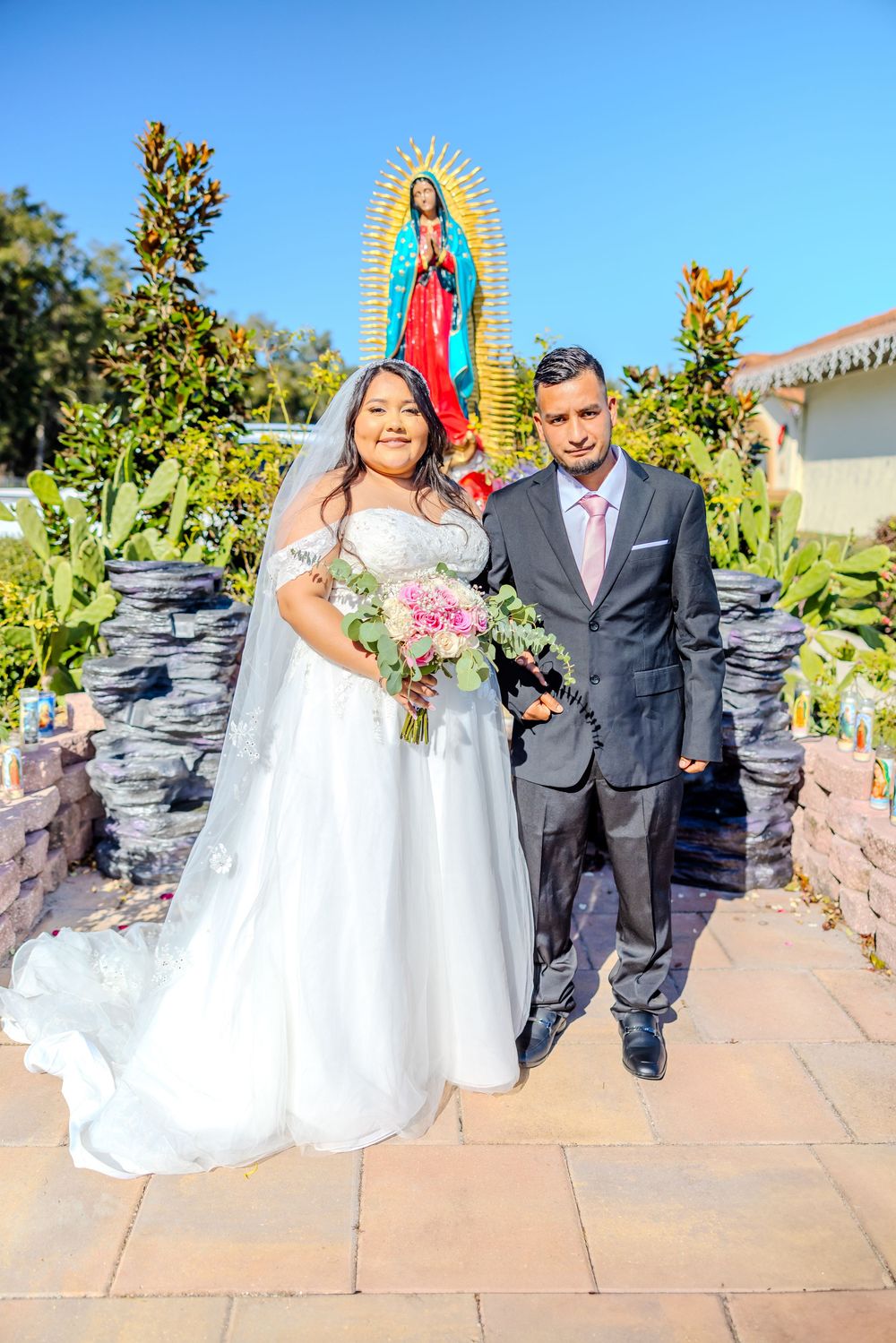 Newlywed couple posing for photos by religious shrine in outdoor garden setting.