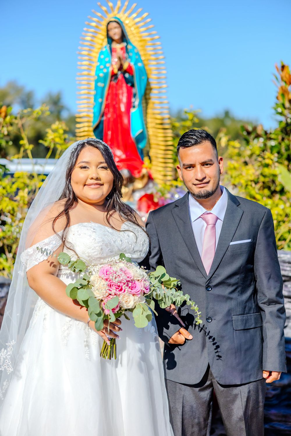 Wedding portraits with couple and religious artwork in sunny garden background.