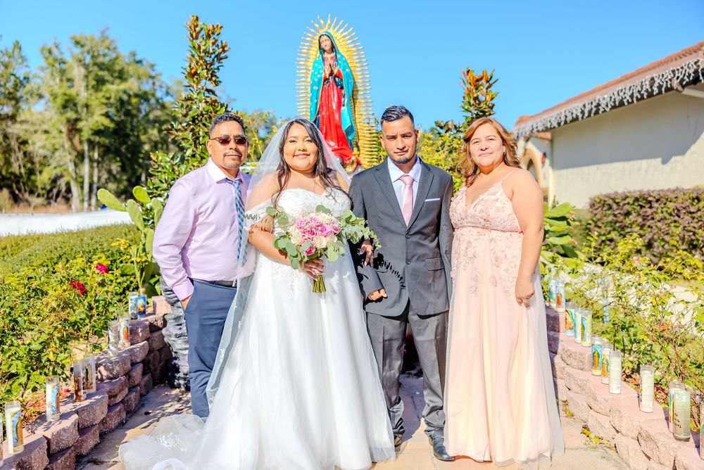 Wedding ceremony group photo with pink bridesmaids dresses and white dress against blue sky backdrop.