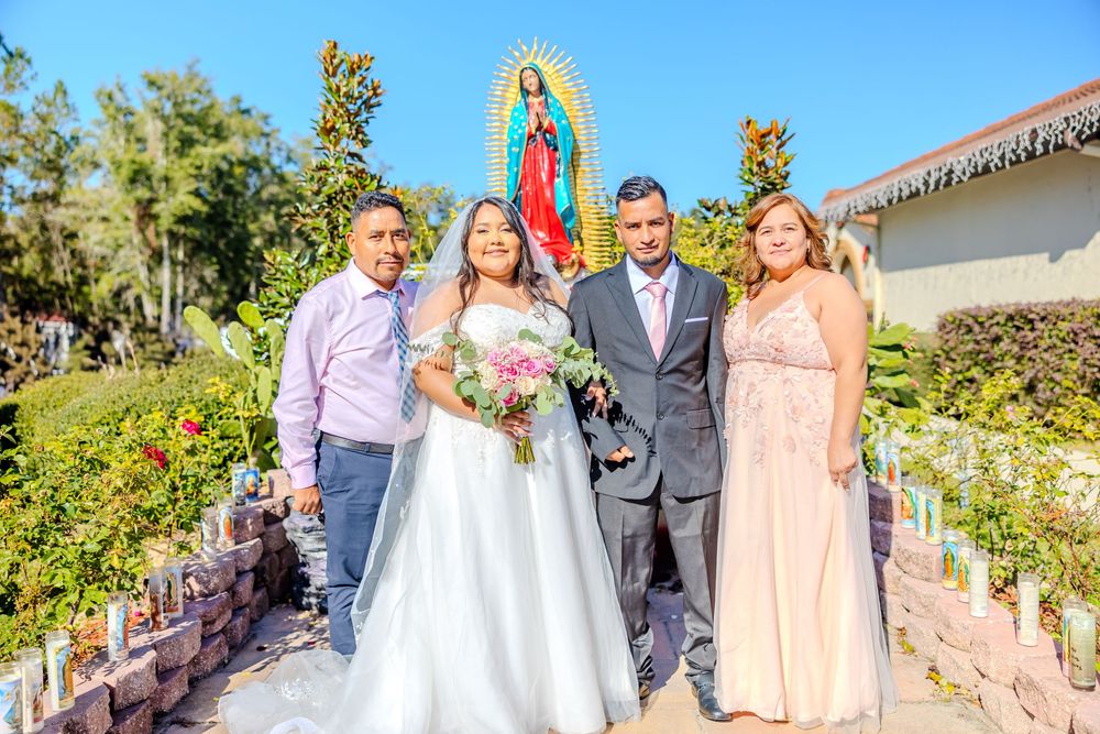 Outdoor wedding photo with bridal party in pink and gray attire near religious statues.