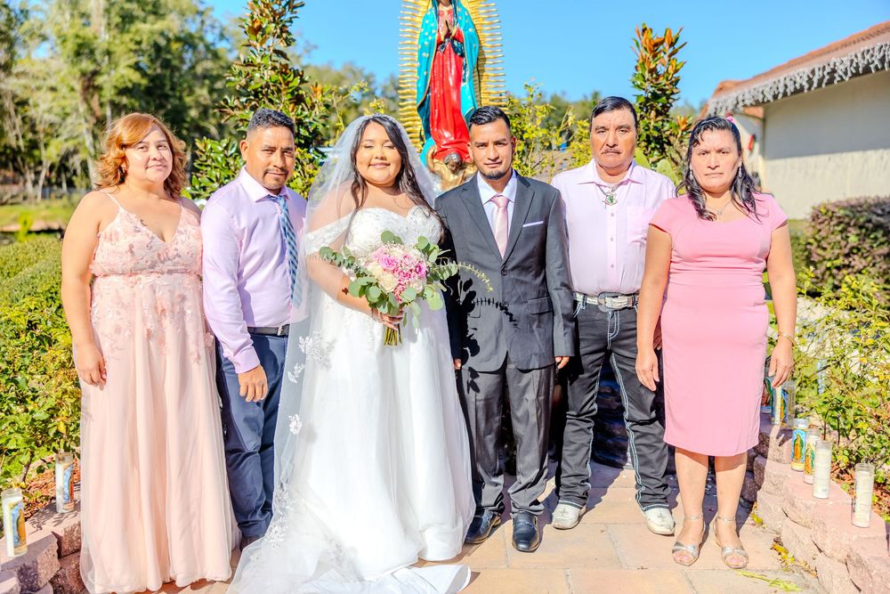 Sunny outdoor wedding photography session with religious statuary and landscaped garden.