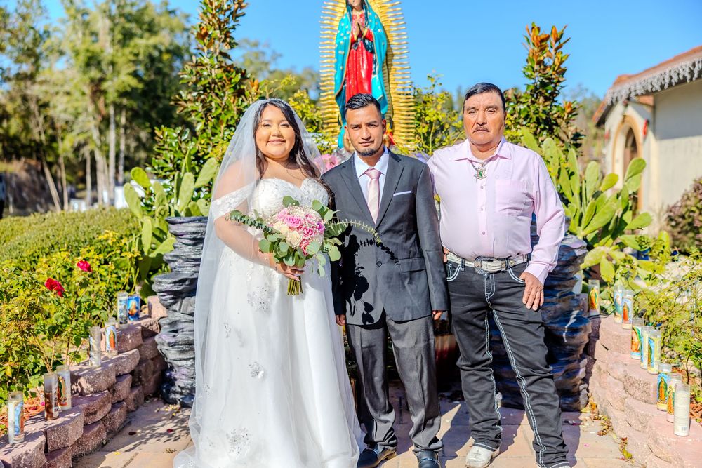 Wedding celebration group photo with religious artwork and natural garden scenery.