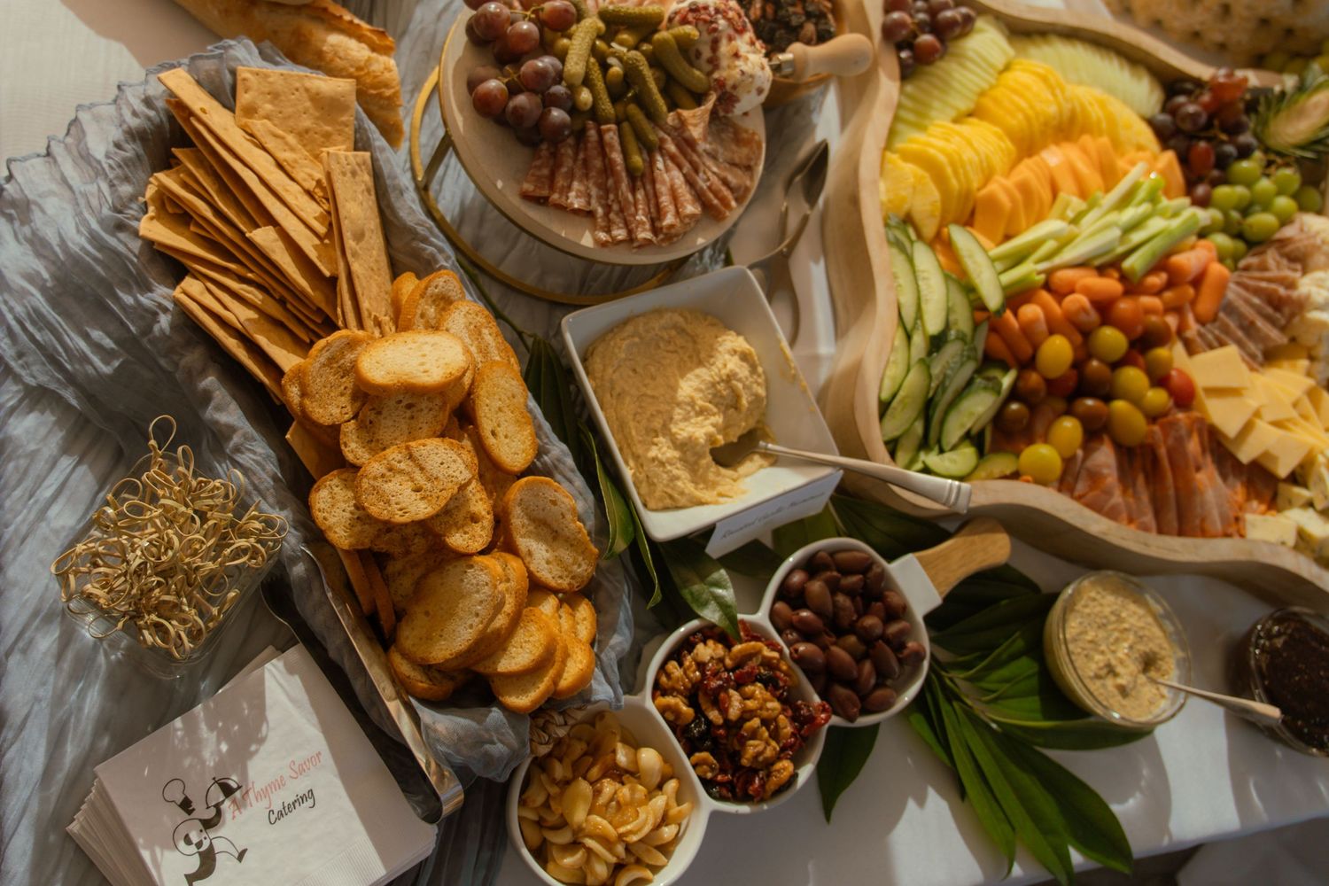 Overhead view of a party platter with fresh vegetables, crackers, nuts, and various dips arranged on a wooden surface.
