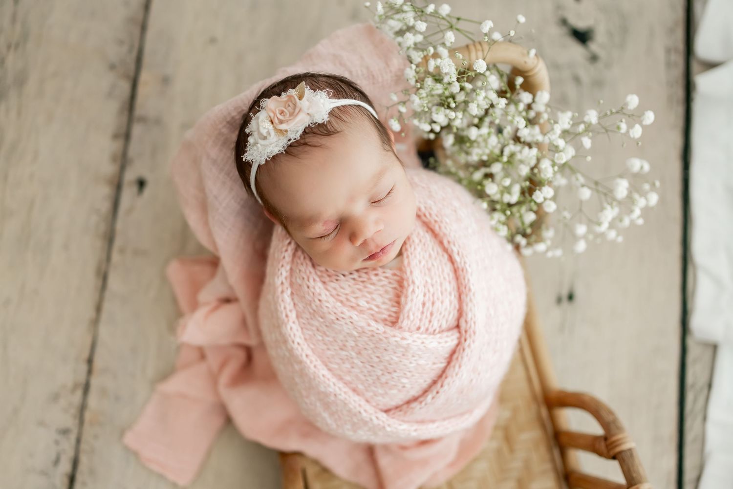 Newborn baby wrapped in soft white knit blanket with tan bow sleeping peacefully.
