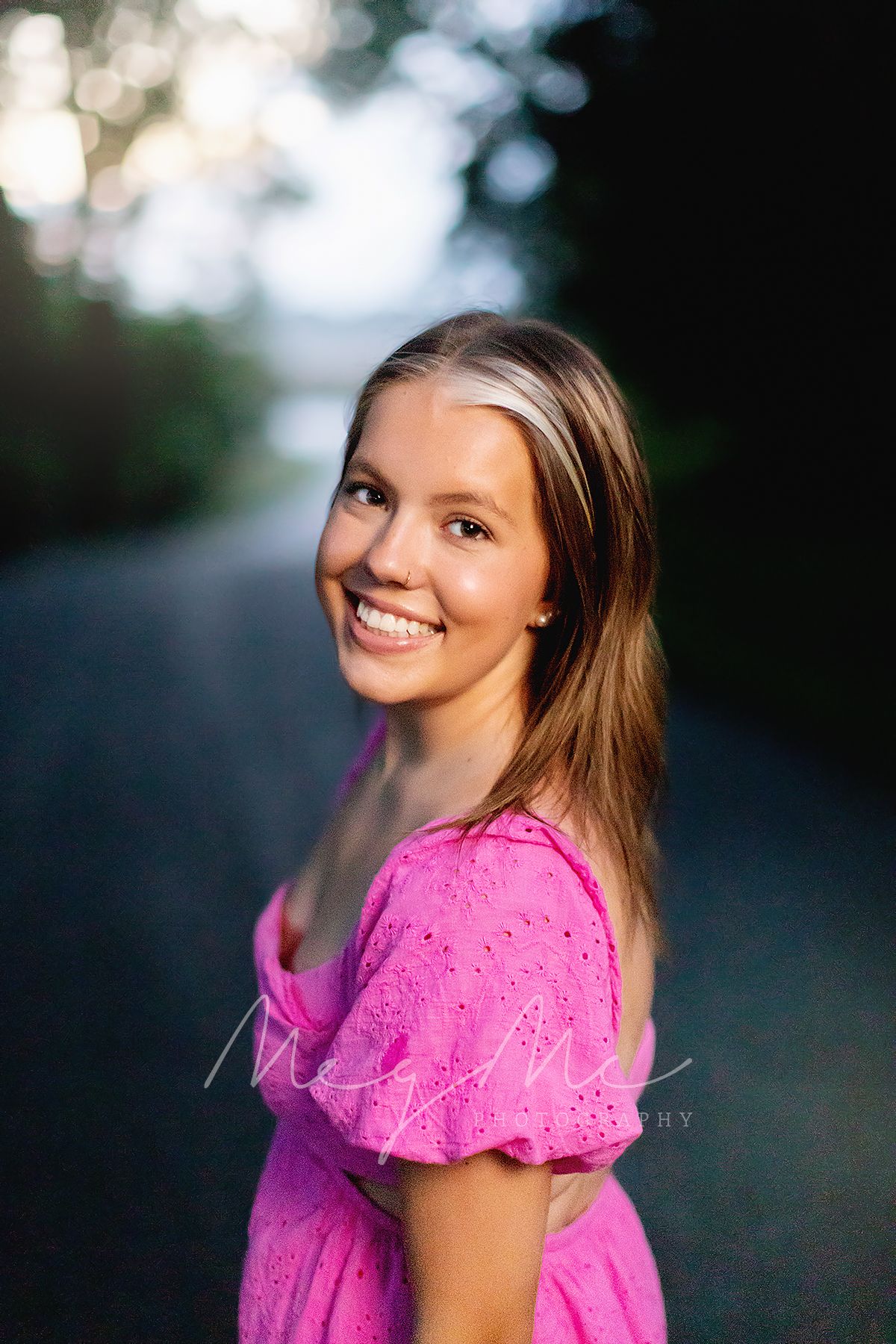 A teen wearing a bright pink dress poses outdoors in natural bokeh lighting during senior pictures with MegMc Photography in Medina, TN