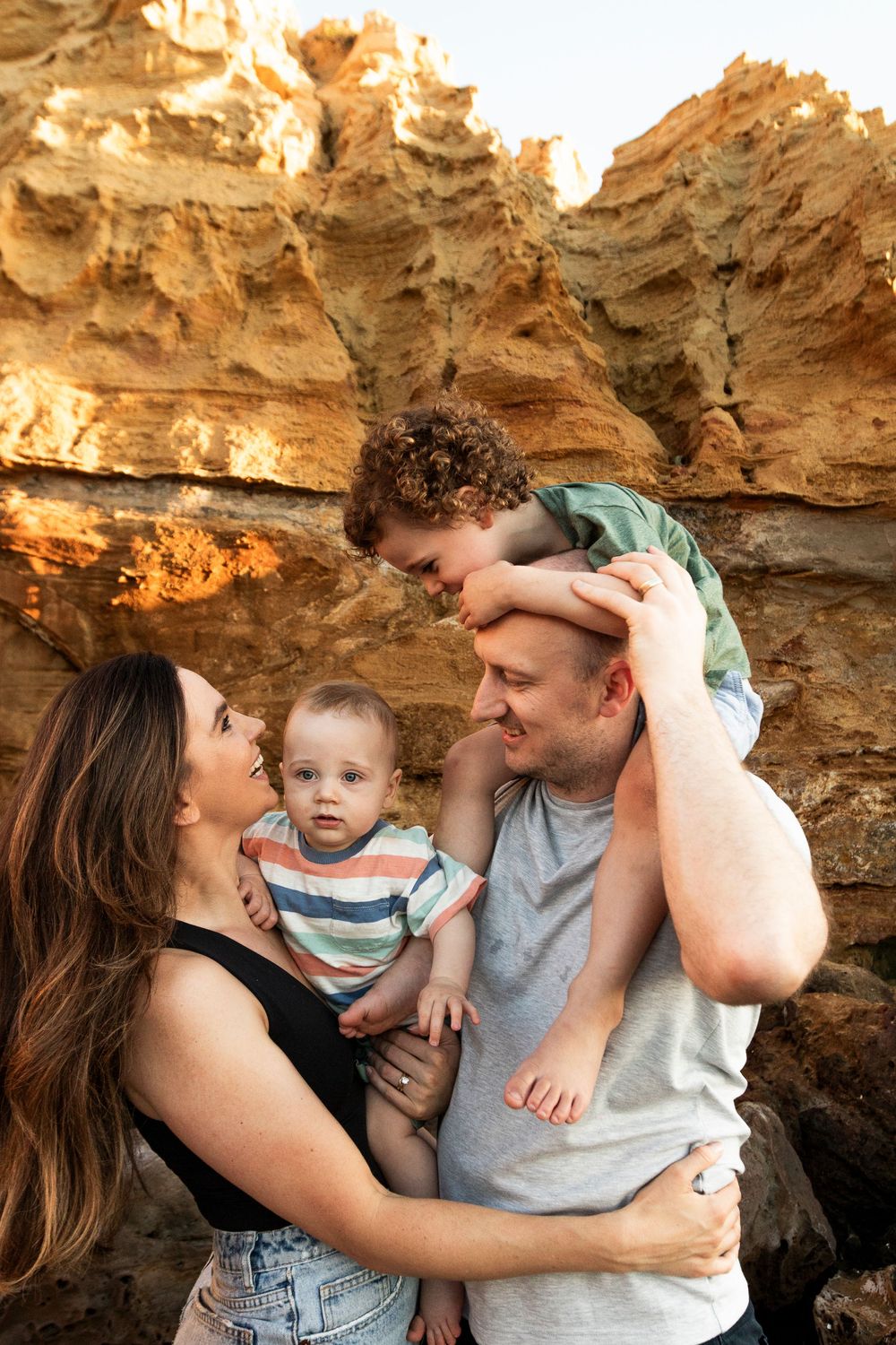 Intimate family moment captured against textured golden rock formations at sunset.