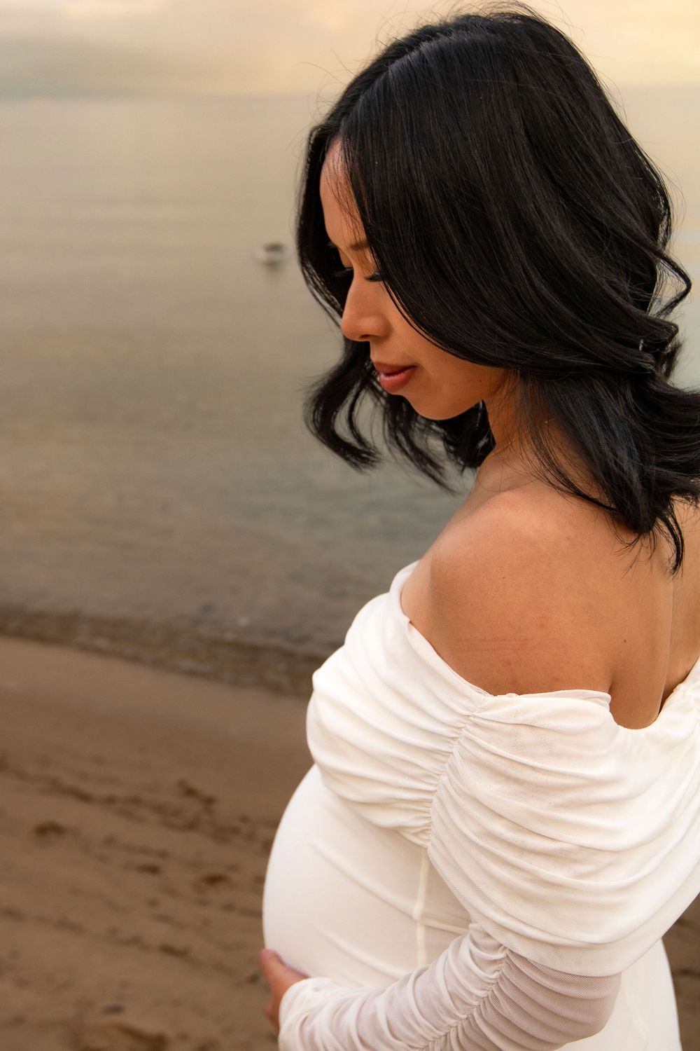 Close-up side view of a woman in white dress with flowing dark hair during beach photoshoot.