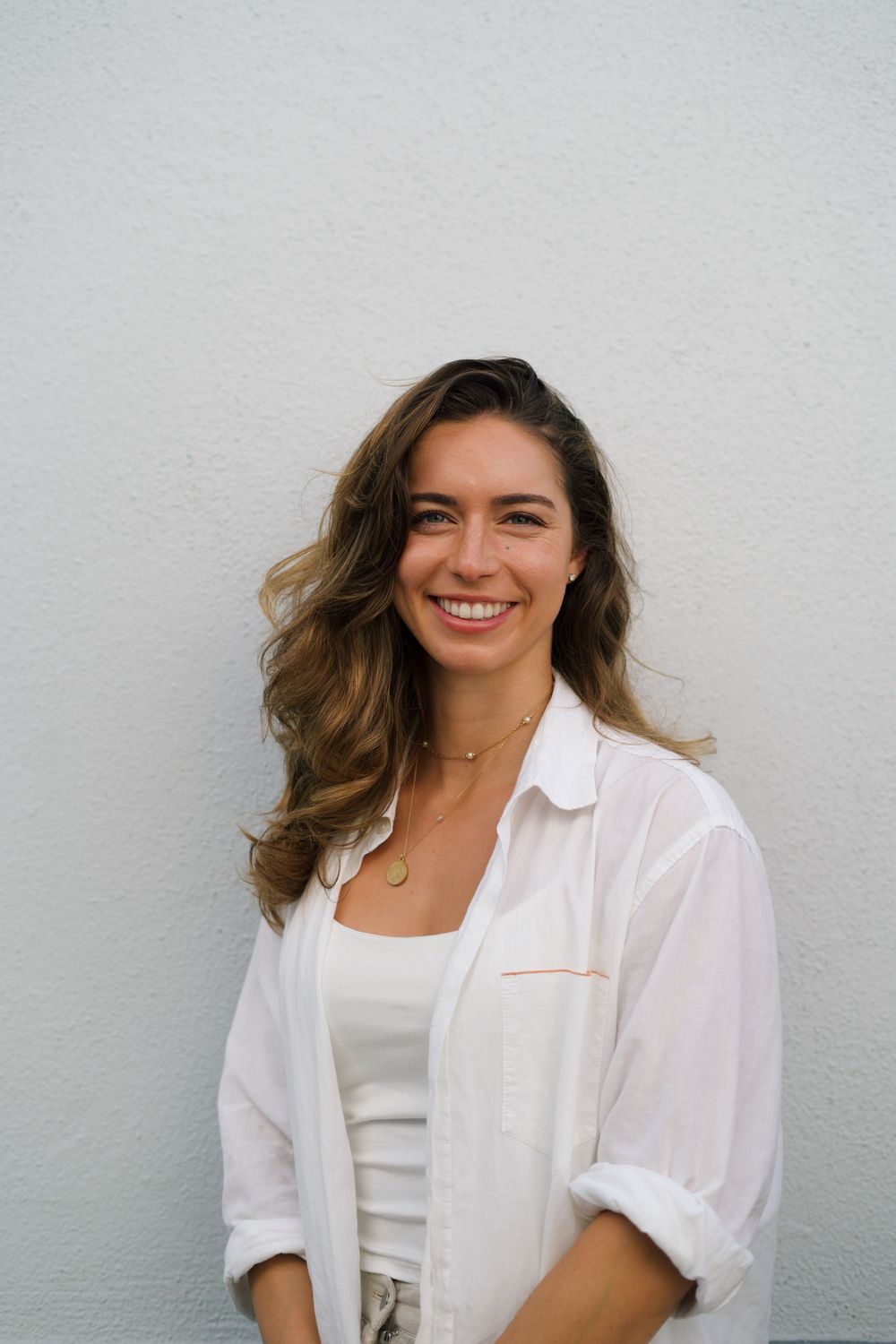 Casual portrait of woman in white button down shirt against plain wall.