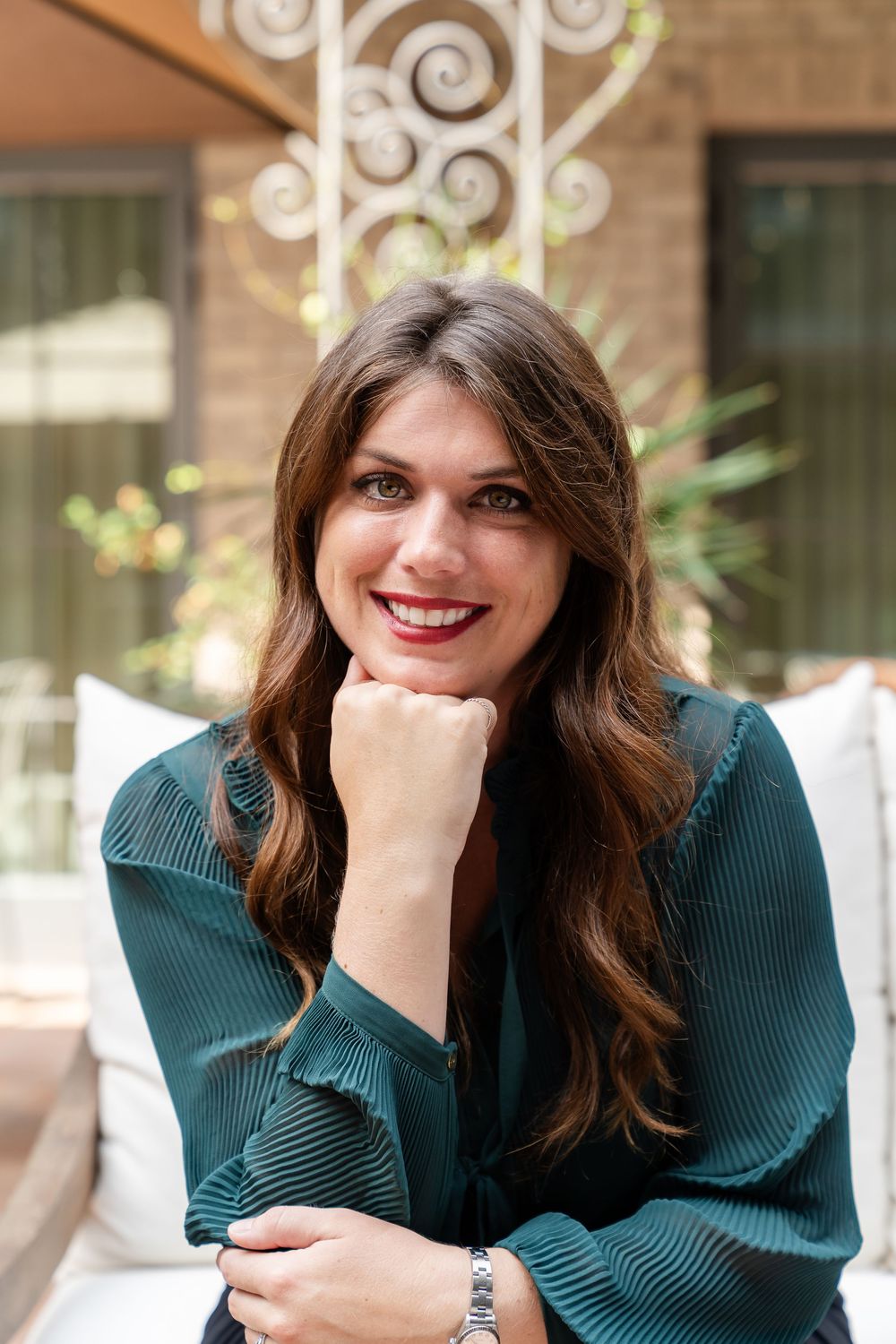 Portrait of woman in teal top seated outdoors with decorative background.