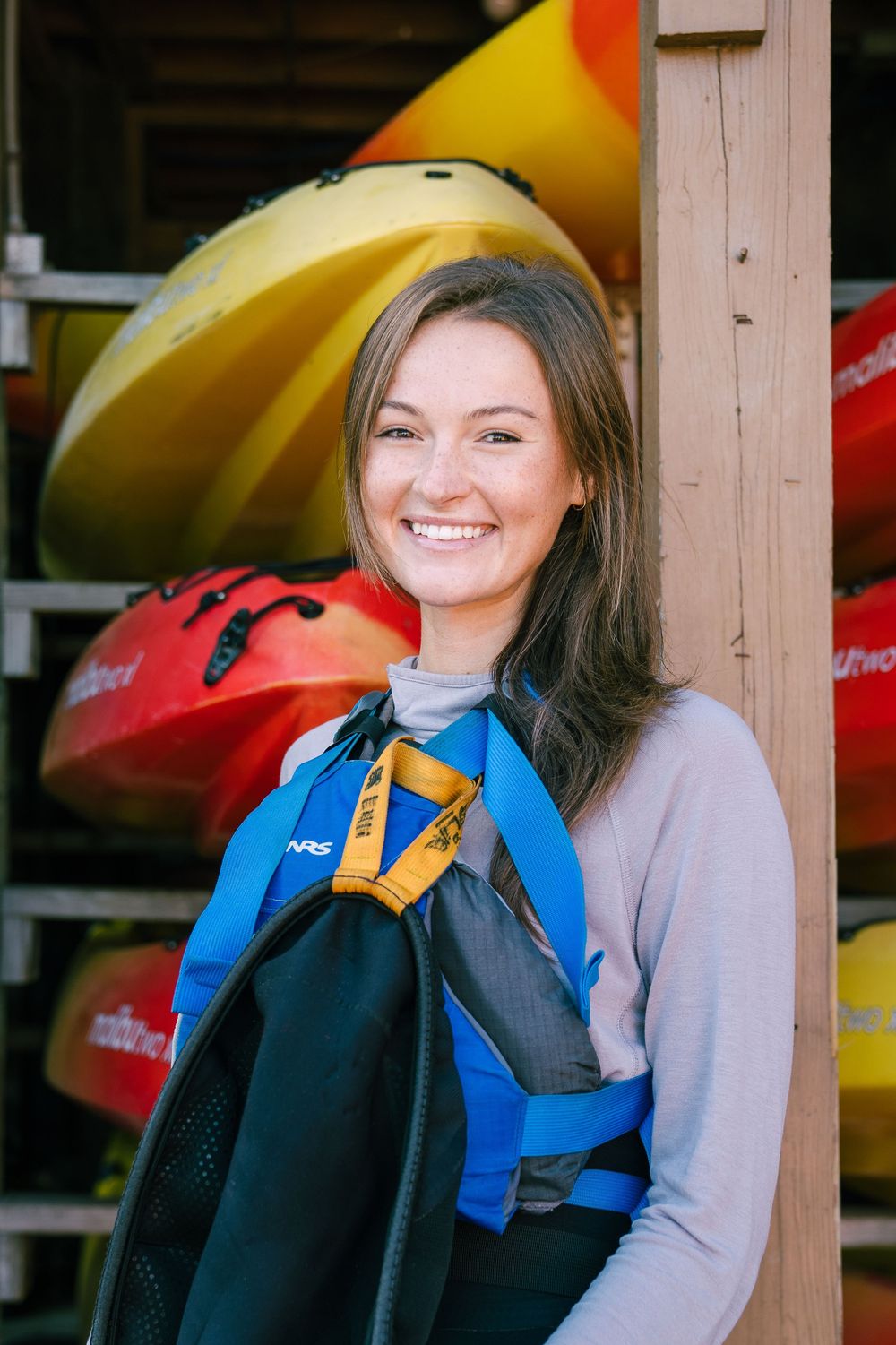 Outdoor portrait at kayak storage rack with colorful boats in background.