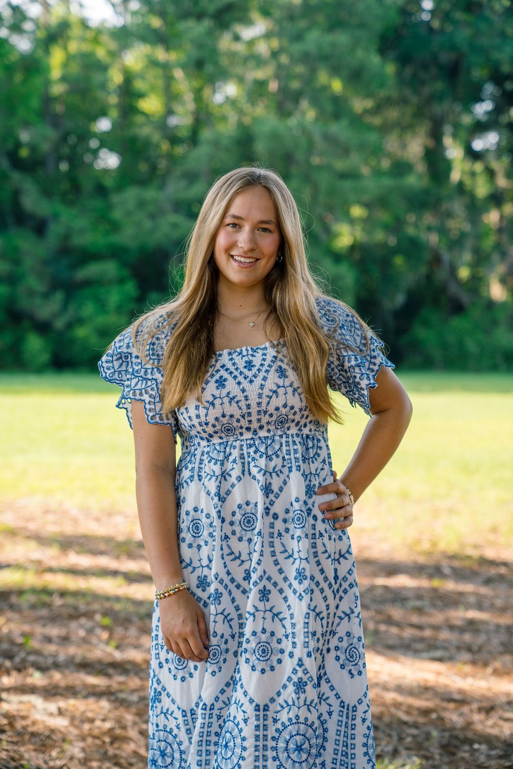 Woman wearing blue and white patterned maxi dress standing in a park setting.