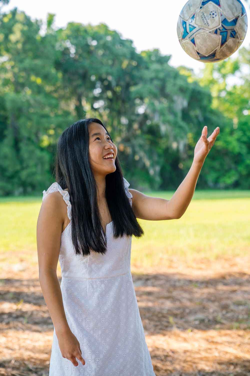Woman in white dress playing with soccer ball outdoors in park setting.
