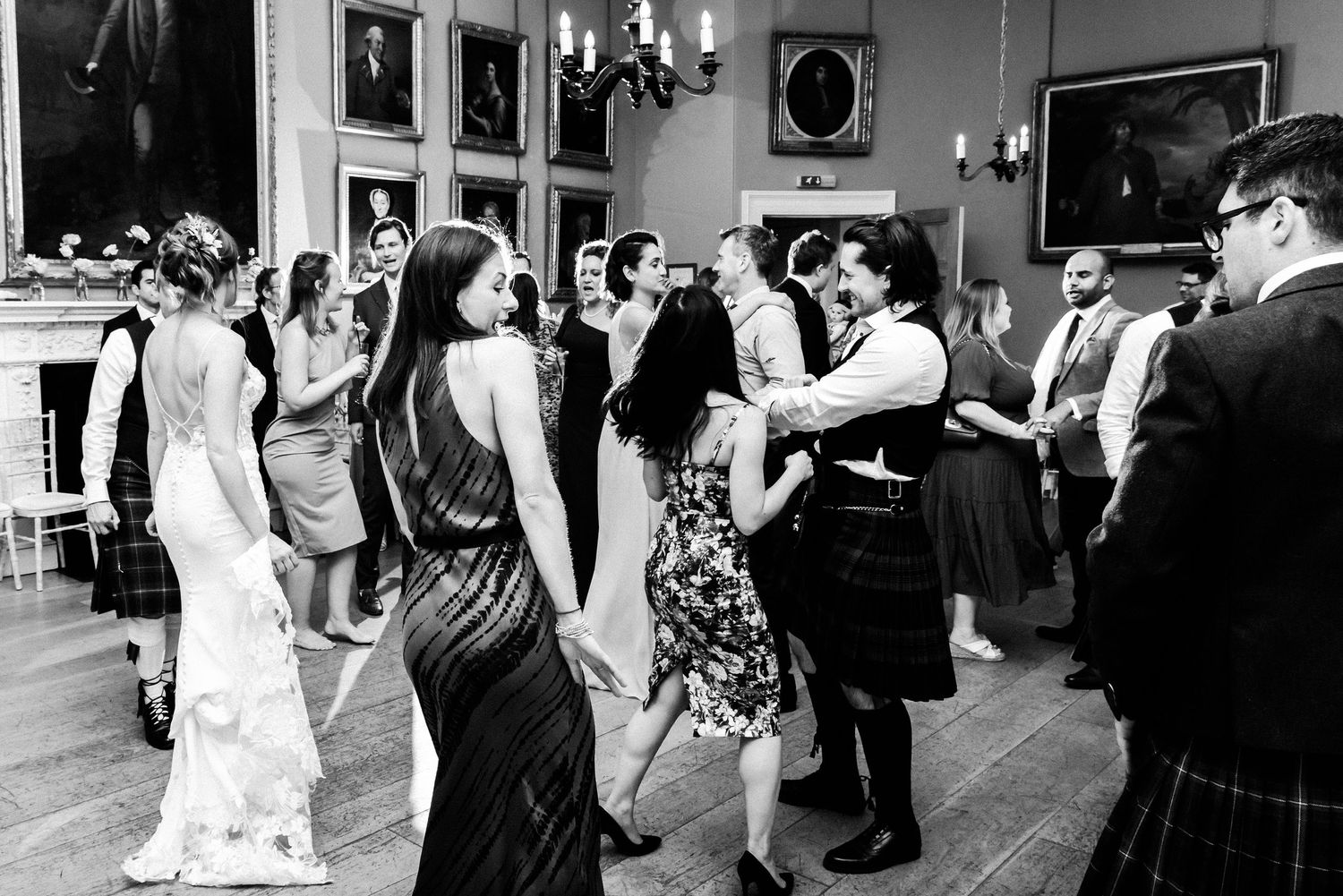 Wedding reception guests dancing on a ballroom floor in black and white photography.